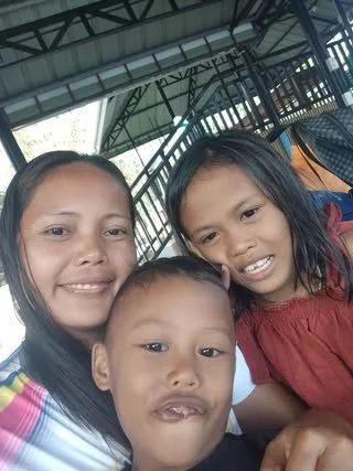 Three children smiling and posing for a photo under a metal pavilion, with trees visible in the background.