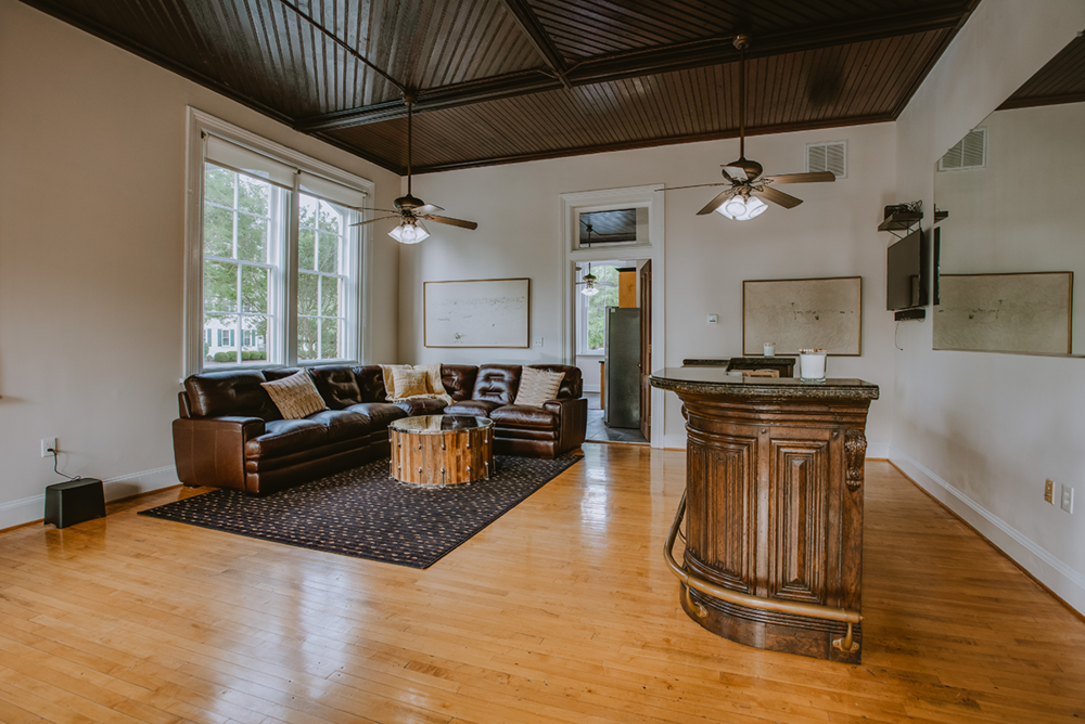 Living room with large window, brown leather sectional sofa, wooden coffee table, patterned area rug, and framed artwork on the white walls.