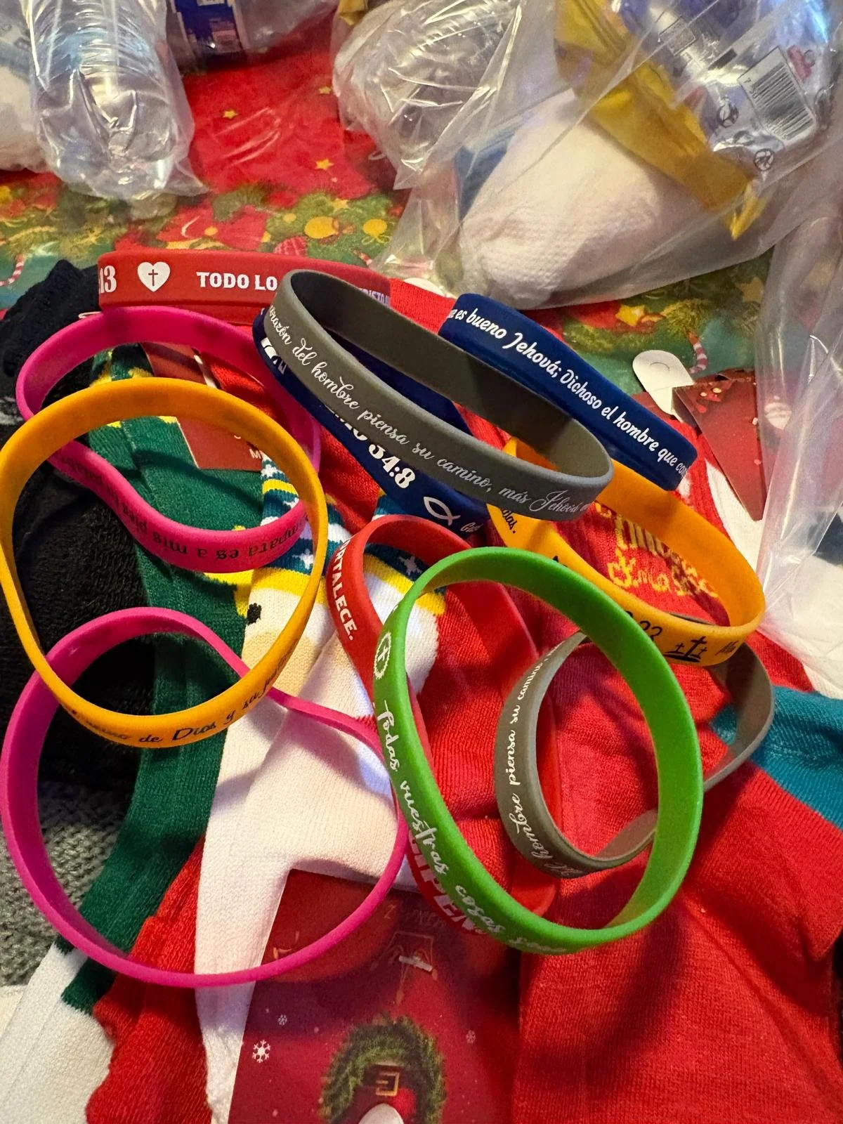 Colorful silicone wristbands with Christian messages and scripture verses on a festive holiday cloth with holiday-themed items around.