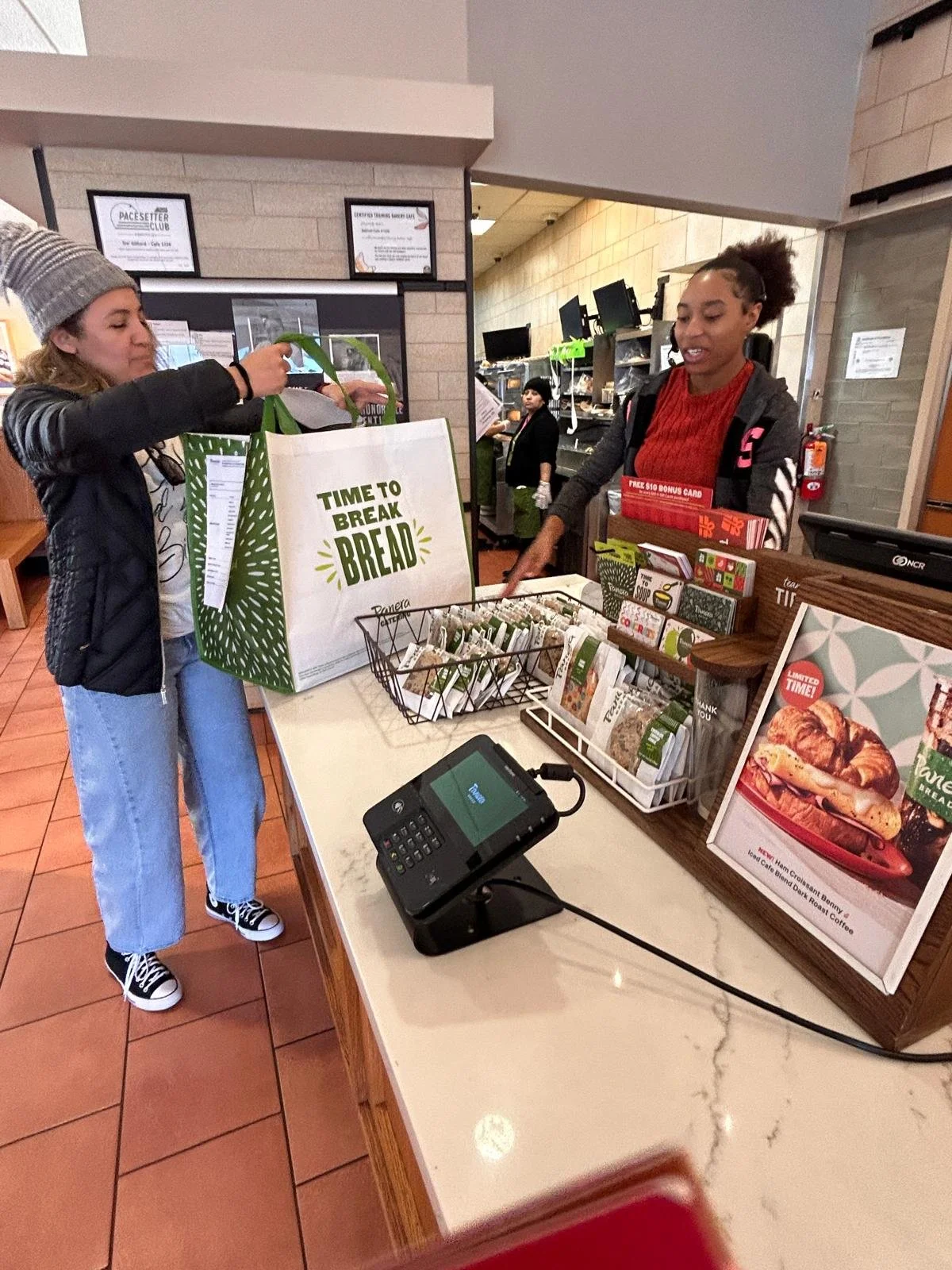 A customer paying at a cafe counter with various coffee bags and promotional signage, while a staff member assists behind the counter.