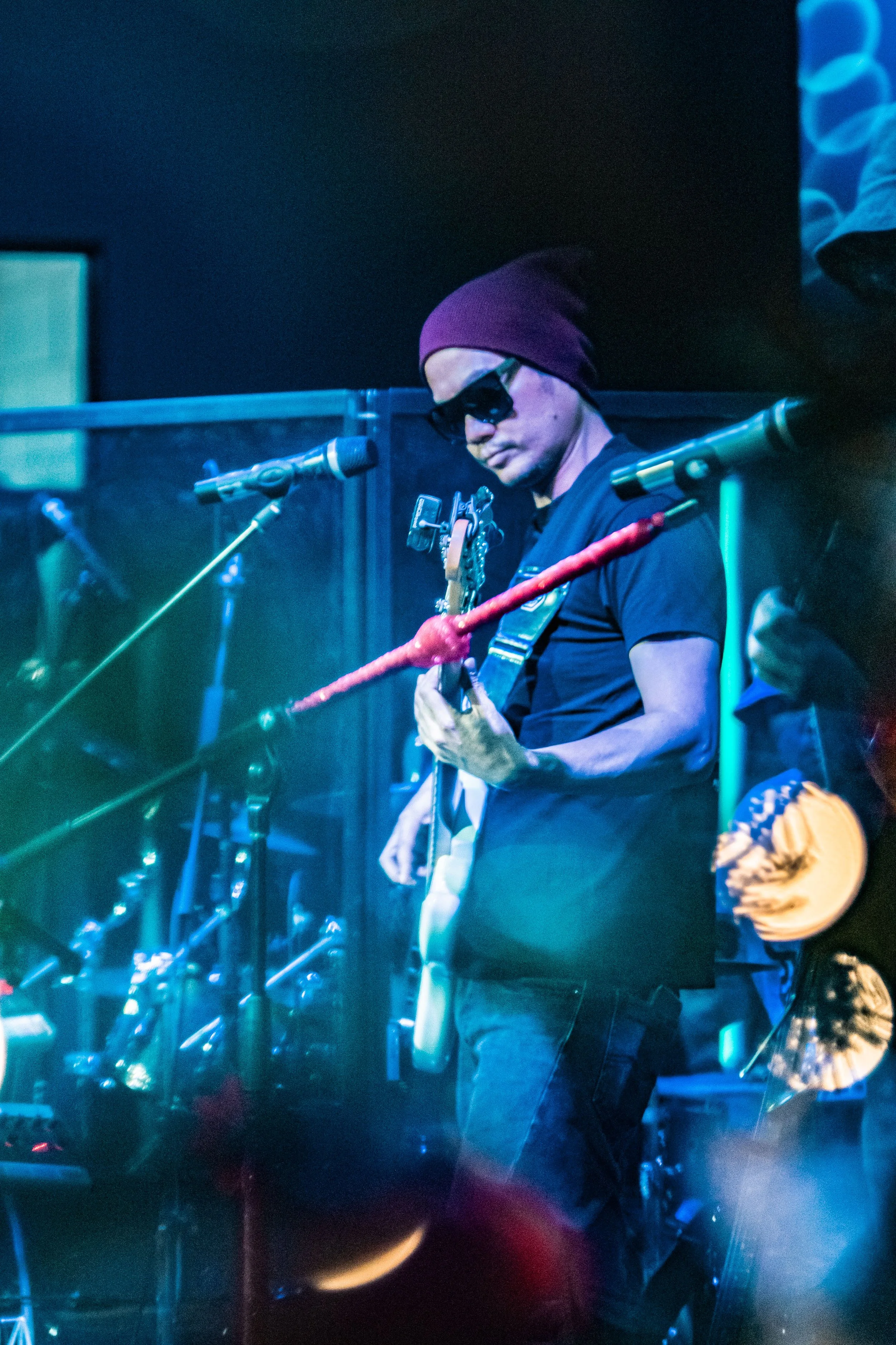 Musician wearing a beanie and sunglasses playing an electric guitar on stage