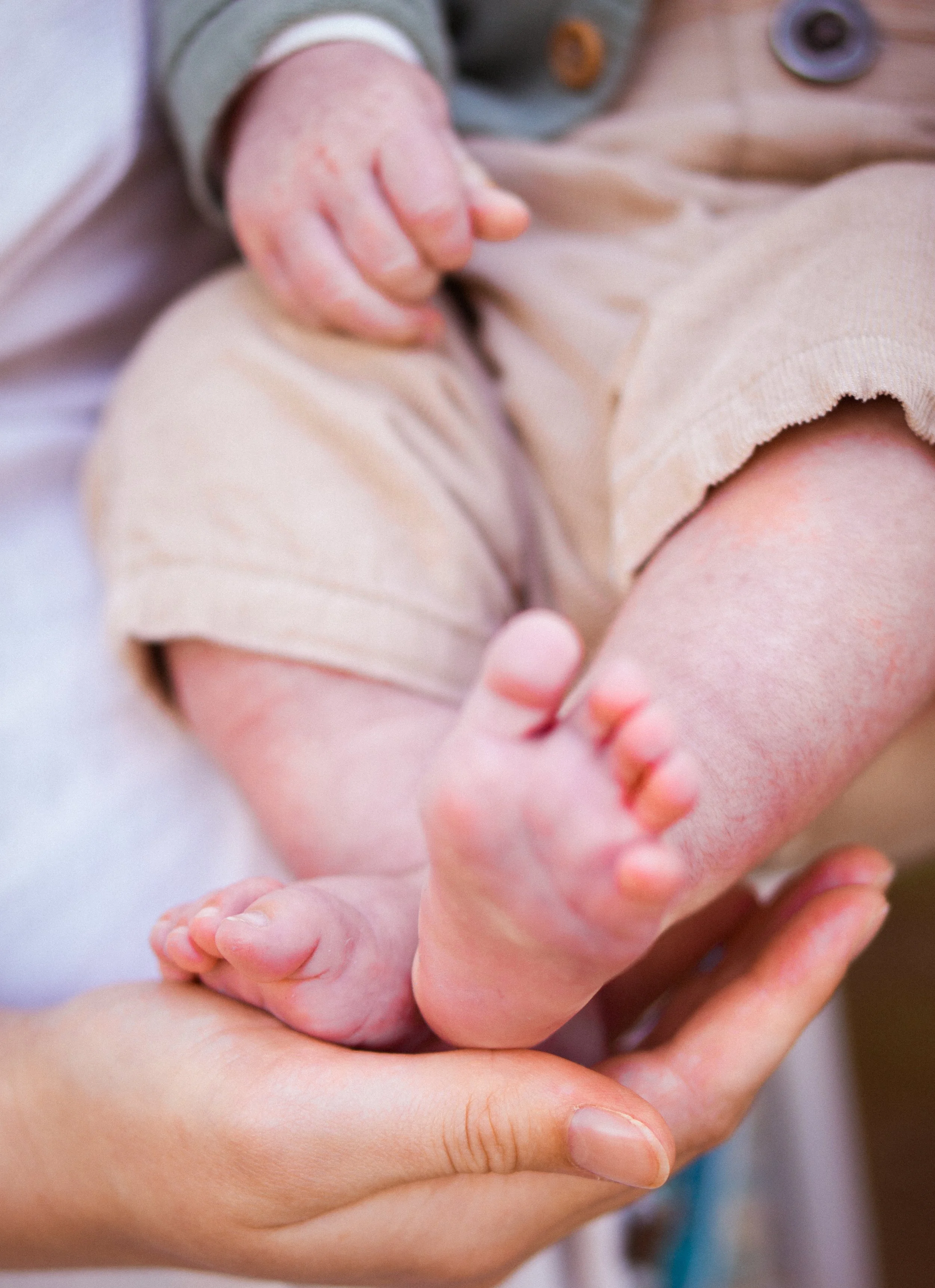 A newborn baby lies in a person's hand, with the person's finger gently touching the baby's toes.