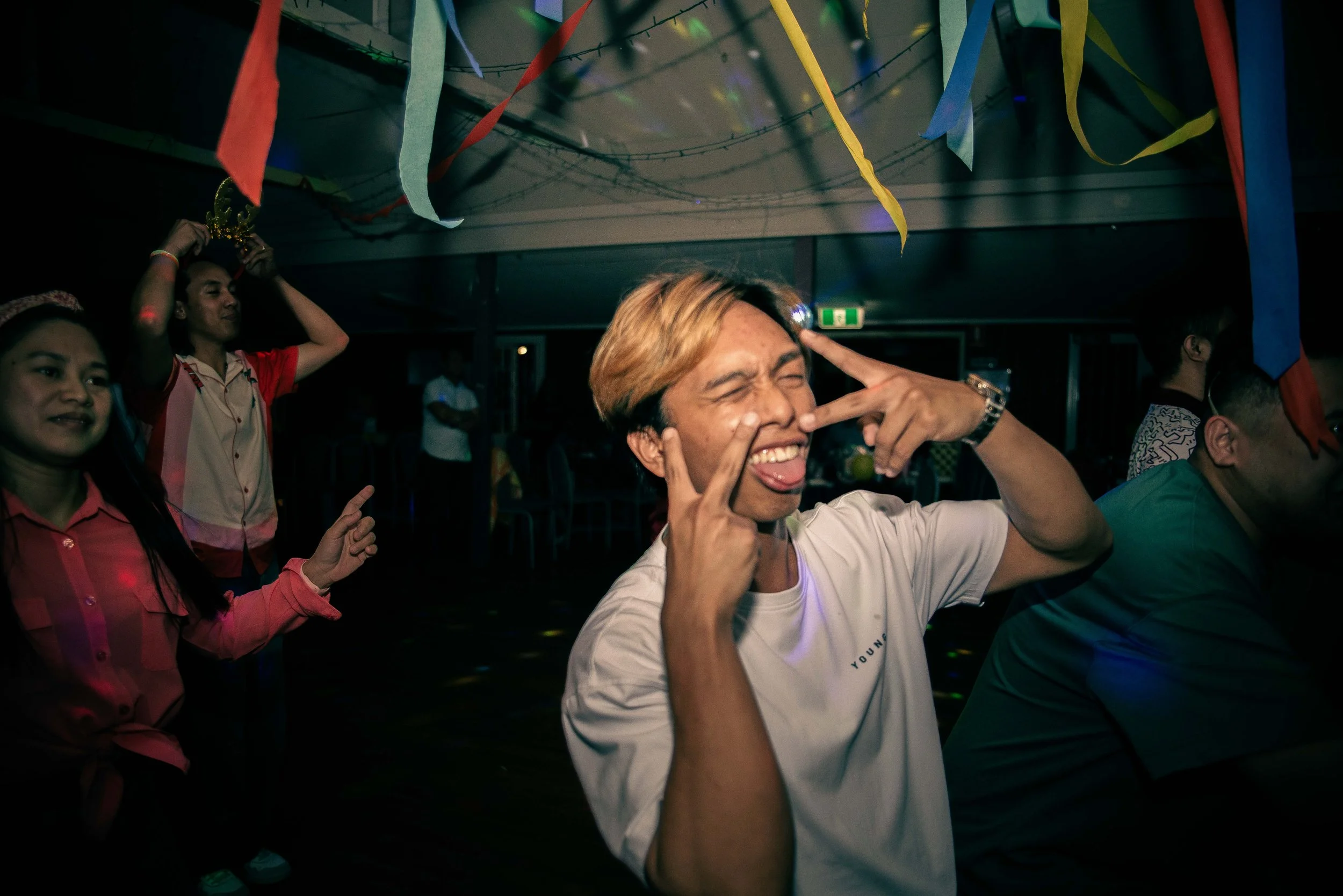 People dancing and celebrating at a party with colorful streamers hanging from the ceiling.
