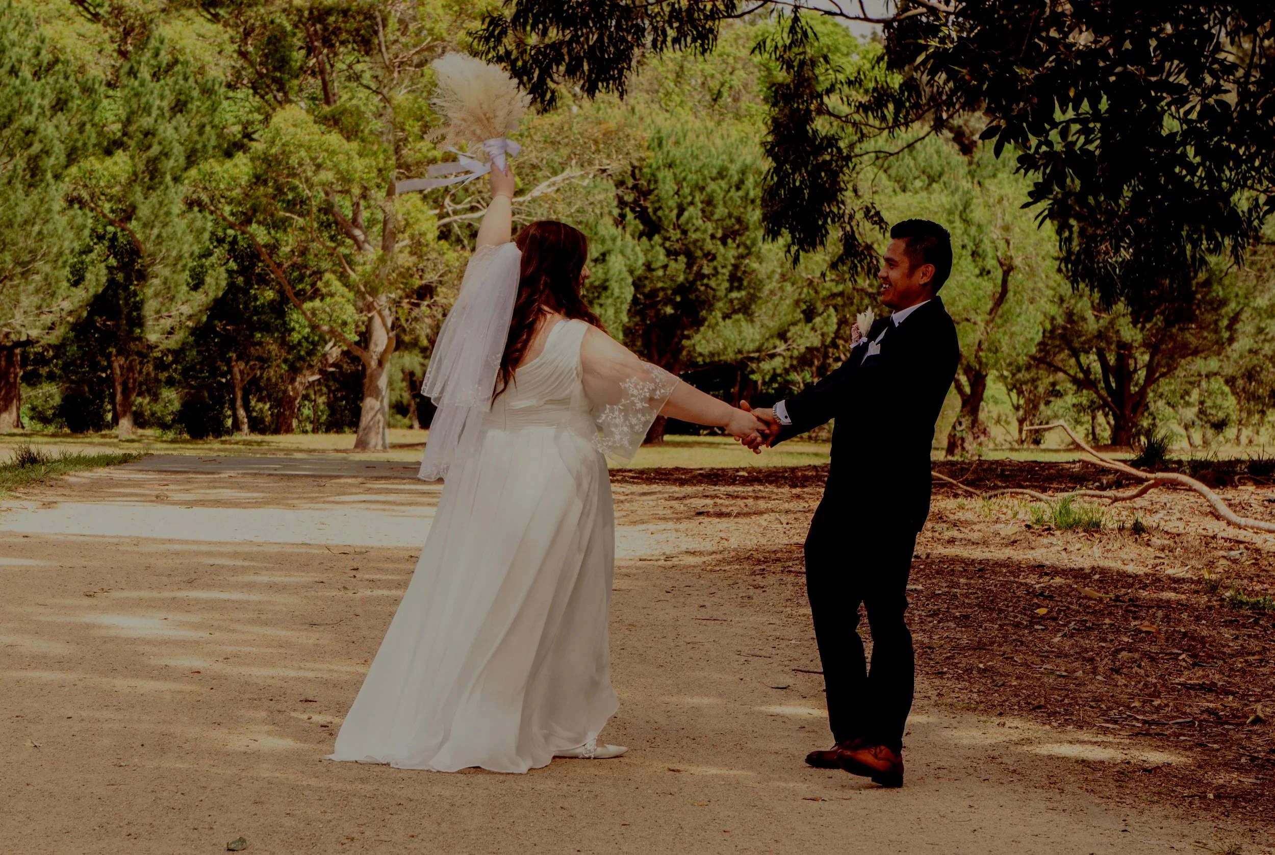 A bride and groom holding hands and smiling outdoors in a wooded area during their wedding.