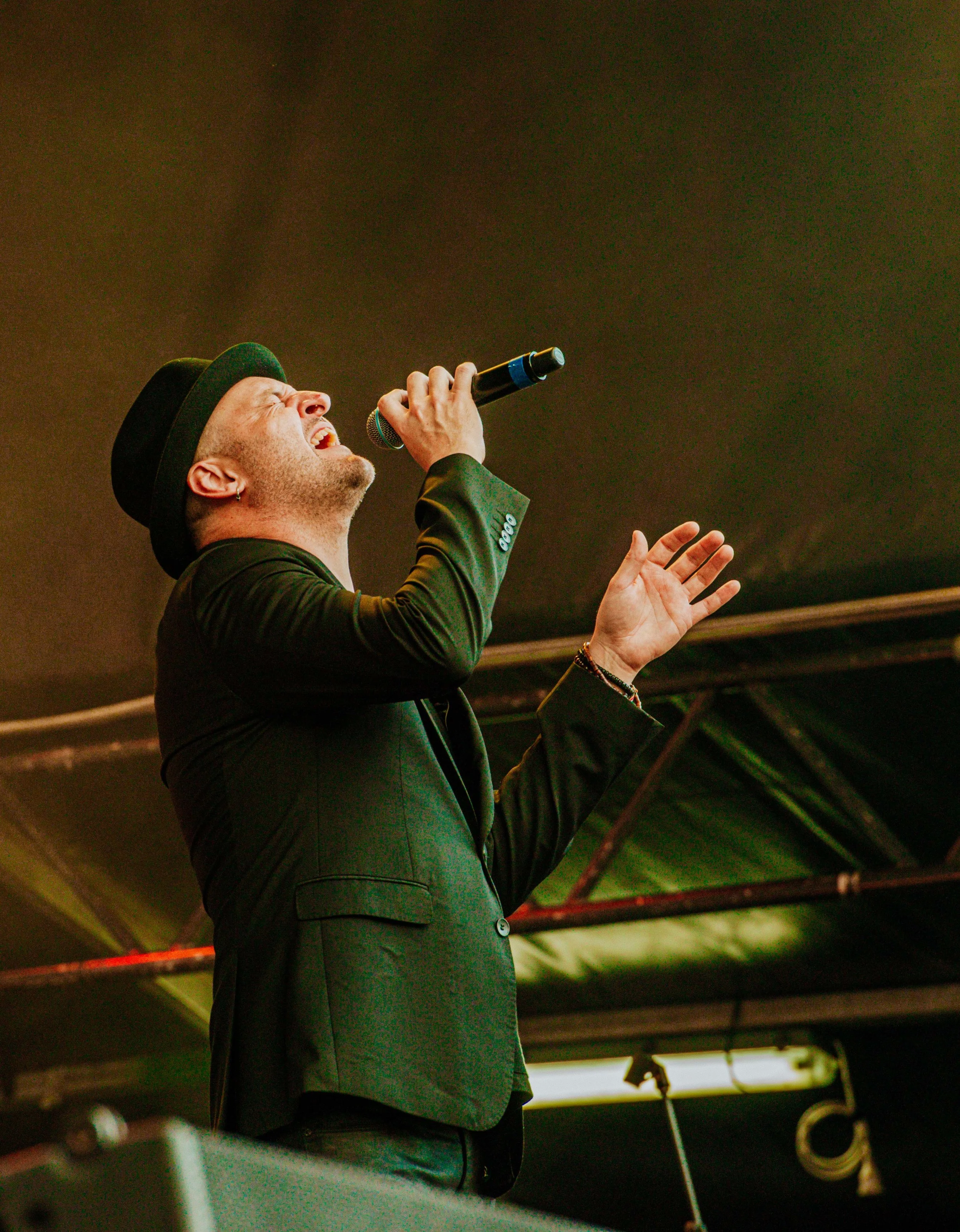 Male singer wearing a suit and hat passionately performing on stage.
