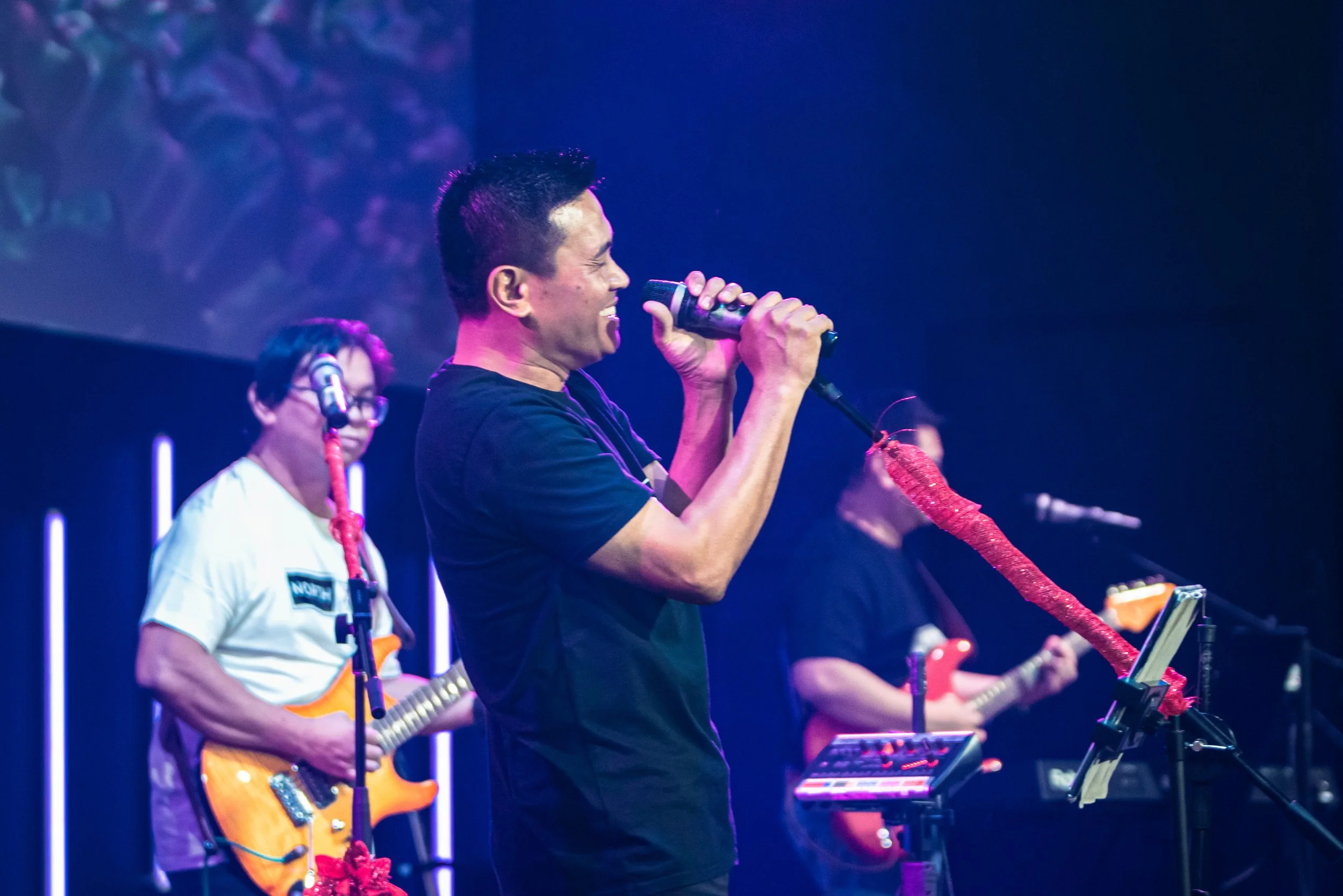 Musicians performing on stage with microphones and instruments under blue and purple lighting.