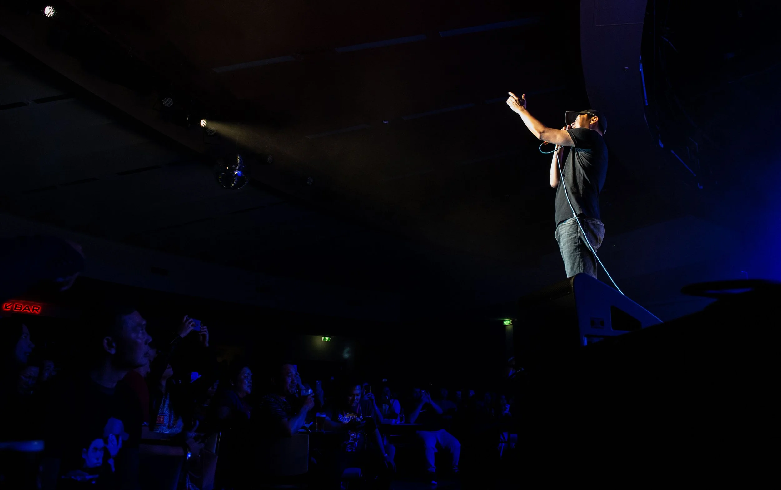 Performer on stage with microphone engaging audience in a dark venue with blue lighting.