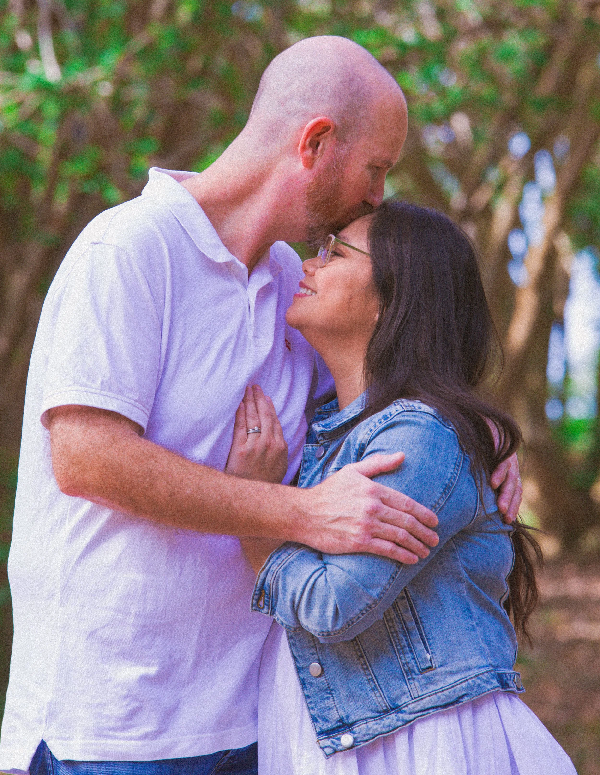 A couple embracing outdoors, the man gently kissing the woman's forehead.