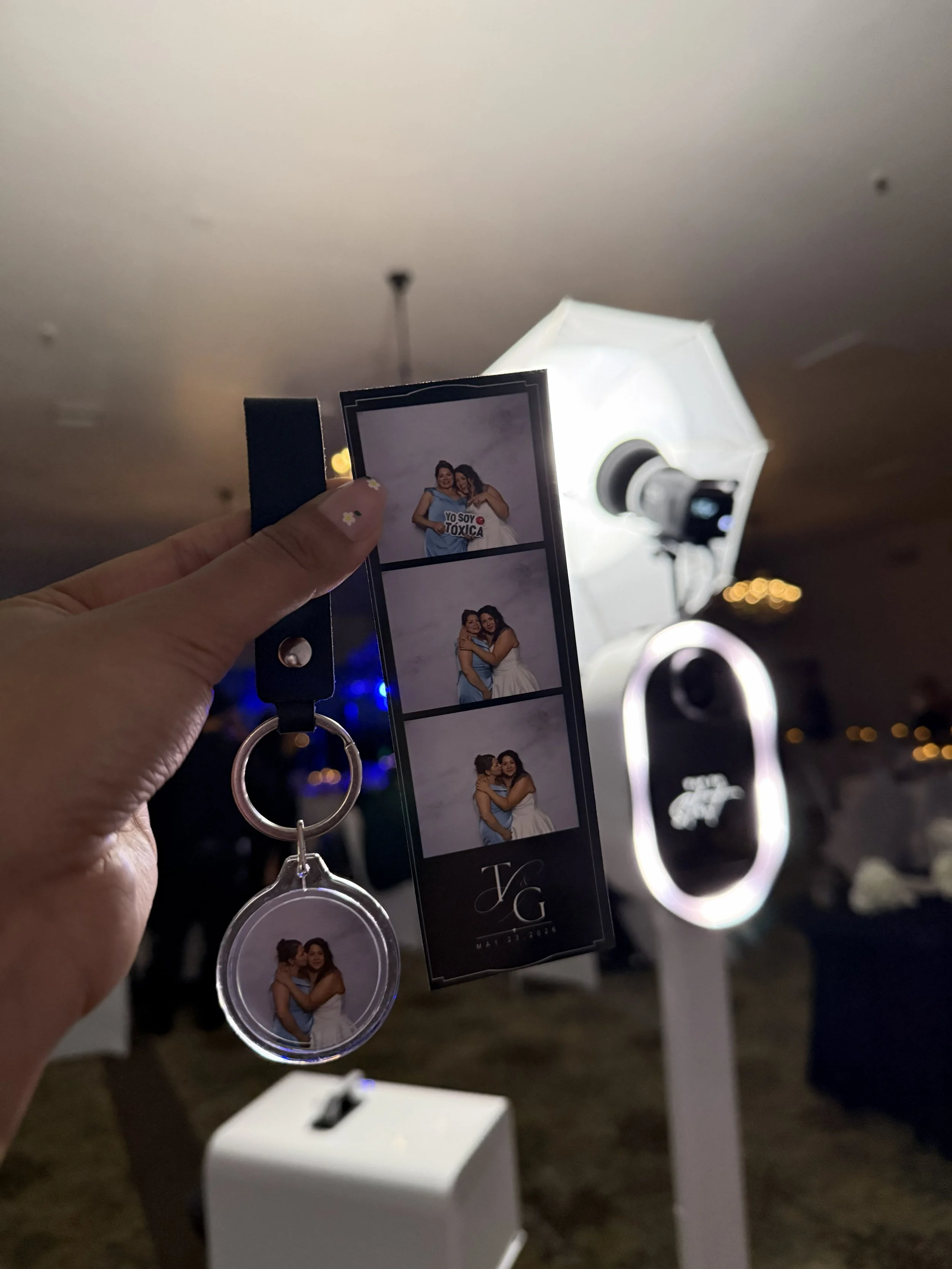Guest holding personalized acrylic photo keychain and custom photo strip next to open air photo booth at wedding reception by Luna Event Rentals in Tri-Cities WA