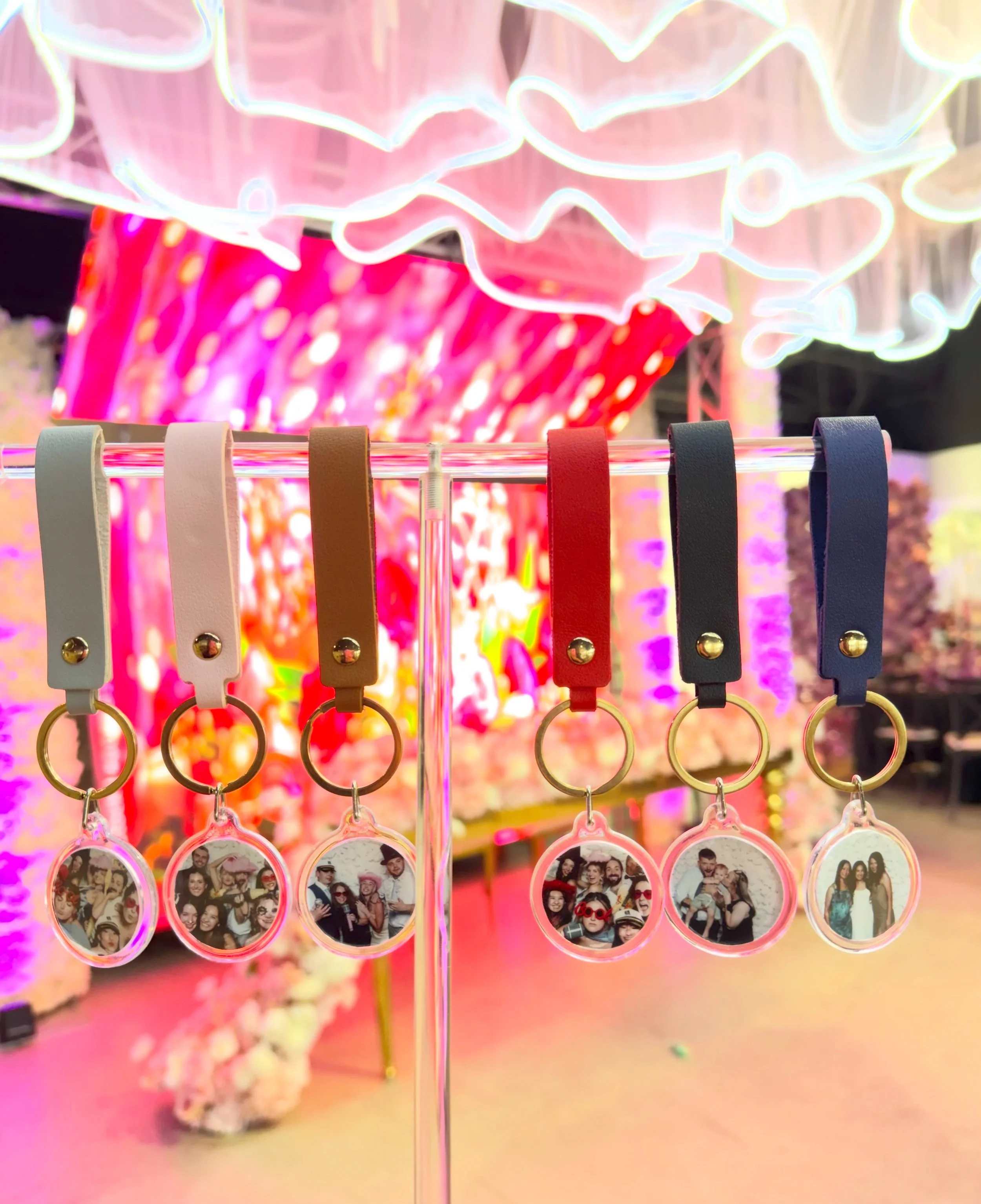 Personalized acrylic photo keychains with colorful leather straps in gray pink brown red and navy displayed on acrylic rack at vibrant quinceañera event by Luna Event Rentals in Tri-Cities WA