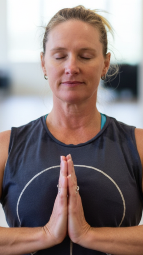 Jennifer Thompson Wholesome Way Practitioner practicing meditation with her hands in a prayer position, eyes closed, in a bright, indoor setting.