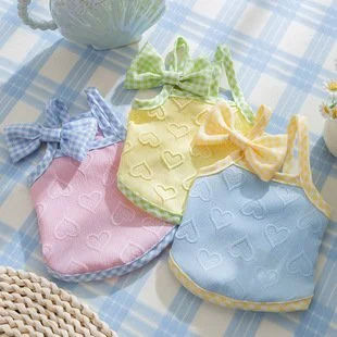 Four fabric bibs in pastel colors with checkered bows, arranged on a checkered cloth.