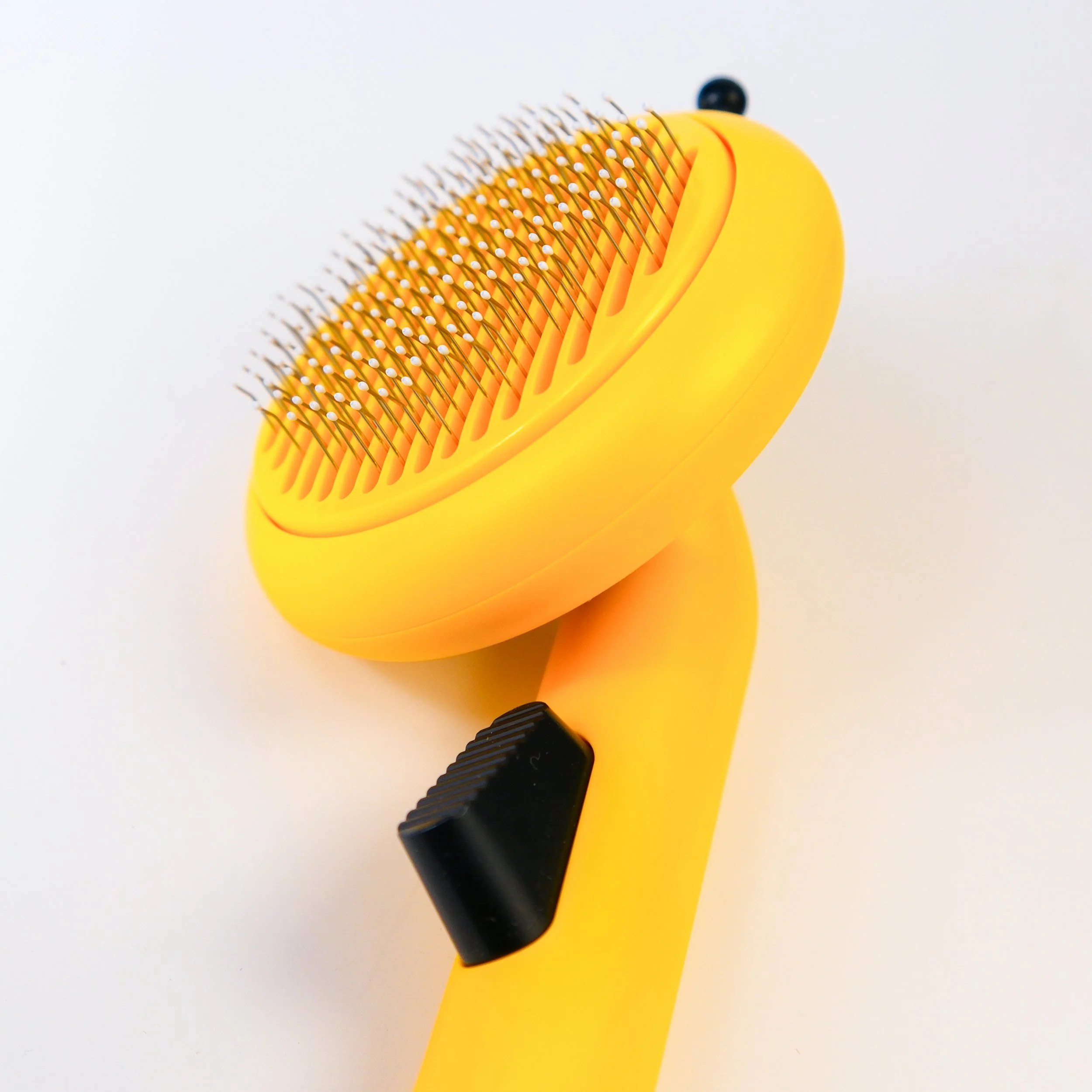 A yellow pet grooming brush with metal bristles and a black adjustable dial on a white background.
