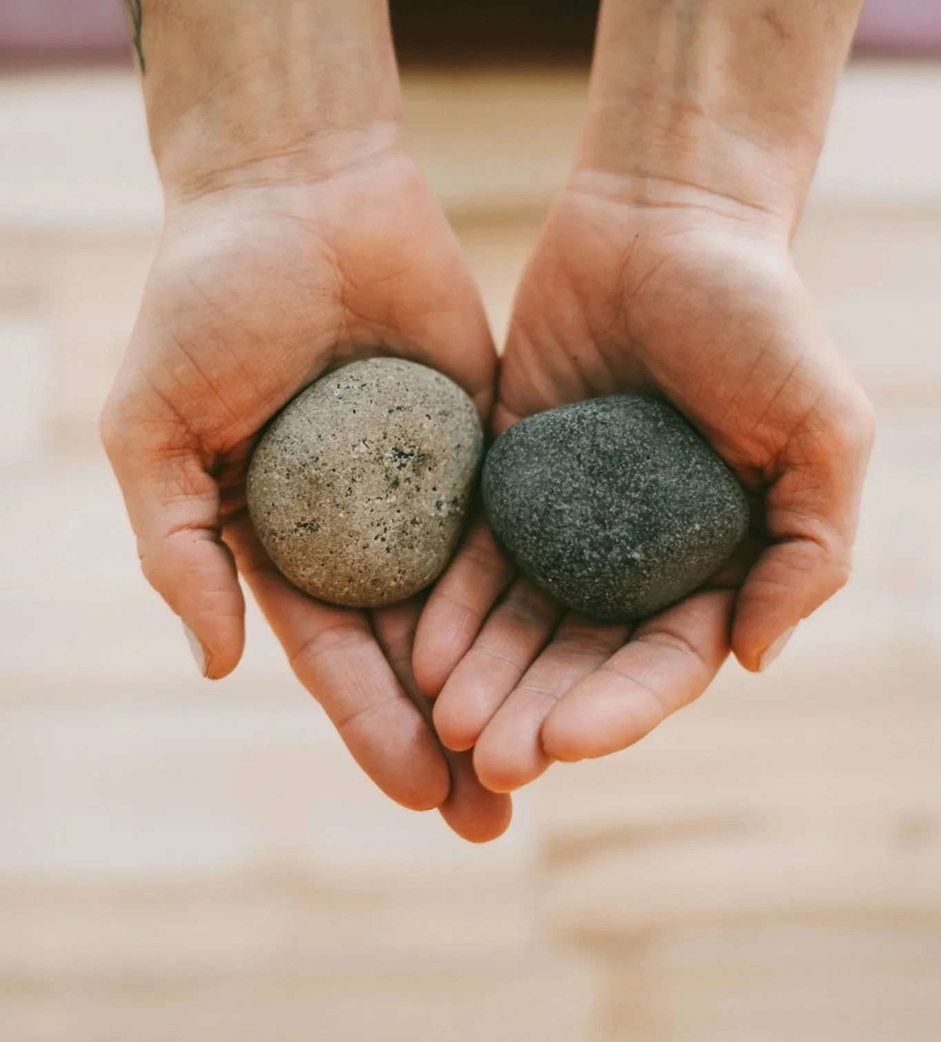 Two hands holding two smooth stones, one light gray and one dark gray, arranged in the shape of a heart.