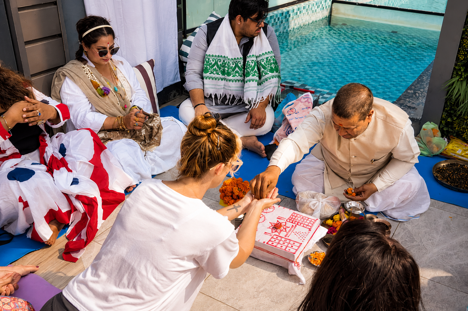 People participating in a Hindu ceremony near a swimming pool, with offerings and traditional attire.