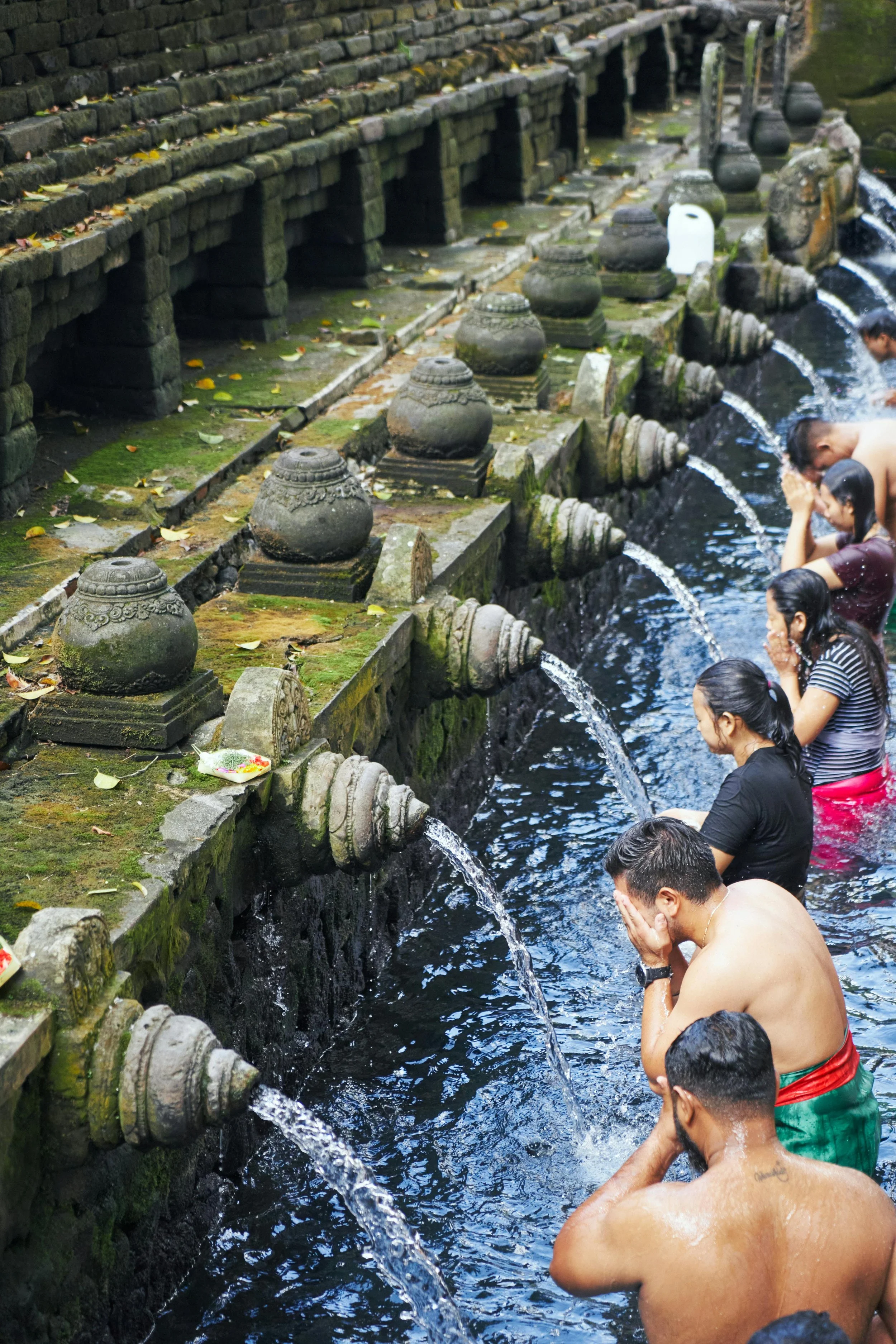 People washing themselves in a row of water spouts in a stone fountain, likely at a religious or cultural site.