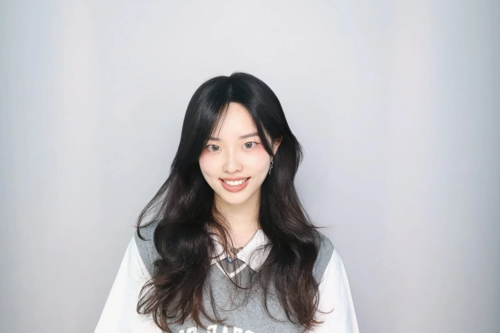 A man with curly dark hair, glasses, and a beard, wearing a black sweater, looking thoughtfully to the side indoors near a plant.