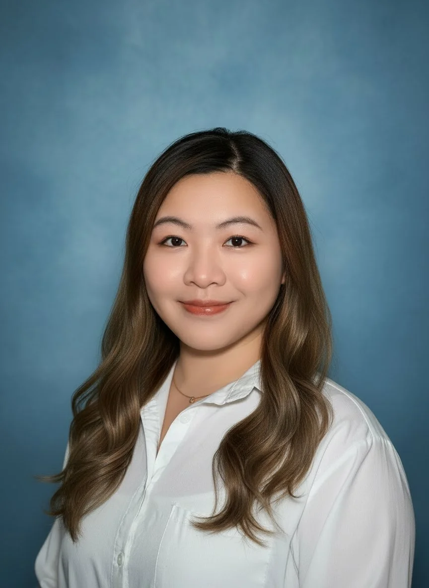 A man with glasses and a nose ring sitting indoors, wearing a dark green sweater, with a blurred background and a plant to the right.