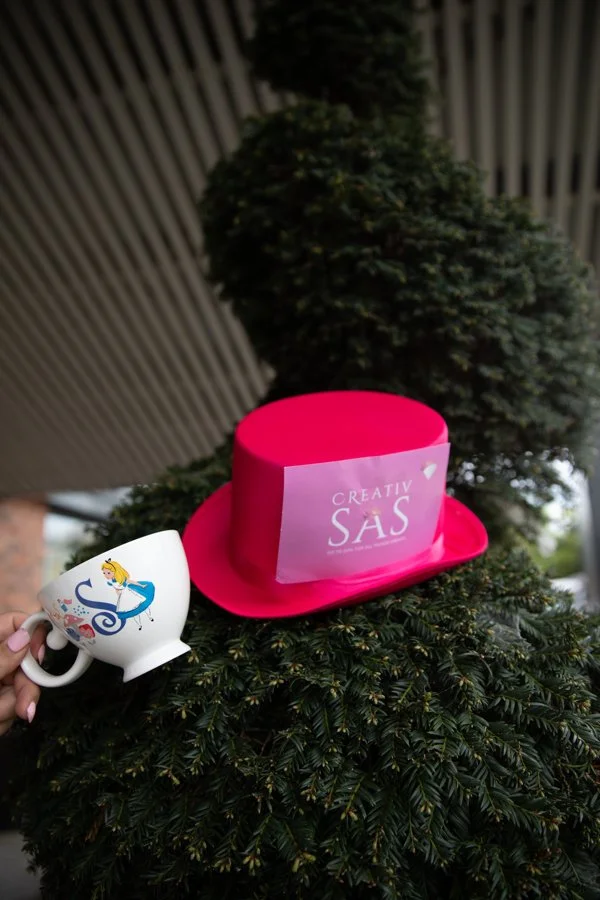 Pink hat with a card reading 'CREATIV SAS' placed on a green pine tree.