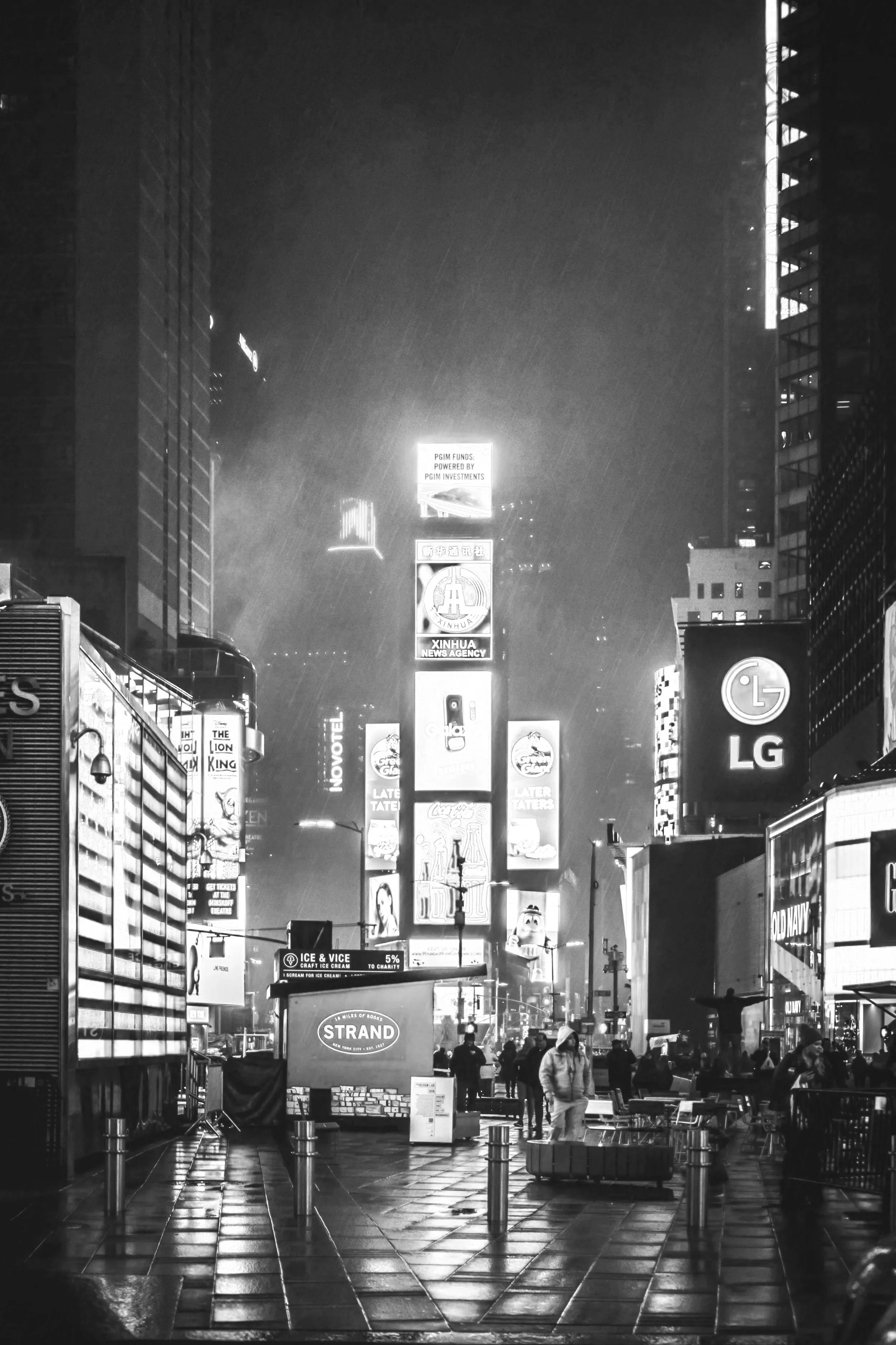 City street scene at night with illuminated billboards, advertisements, and people walking in the rain.