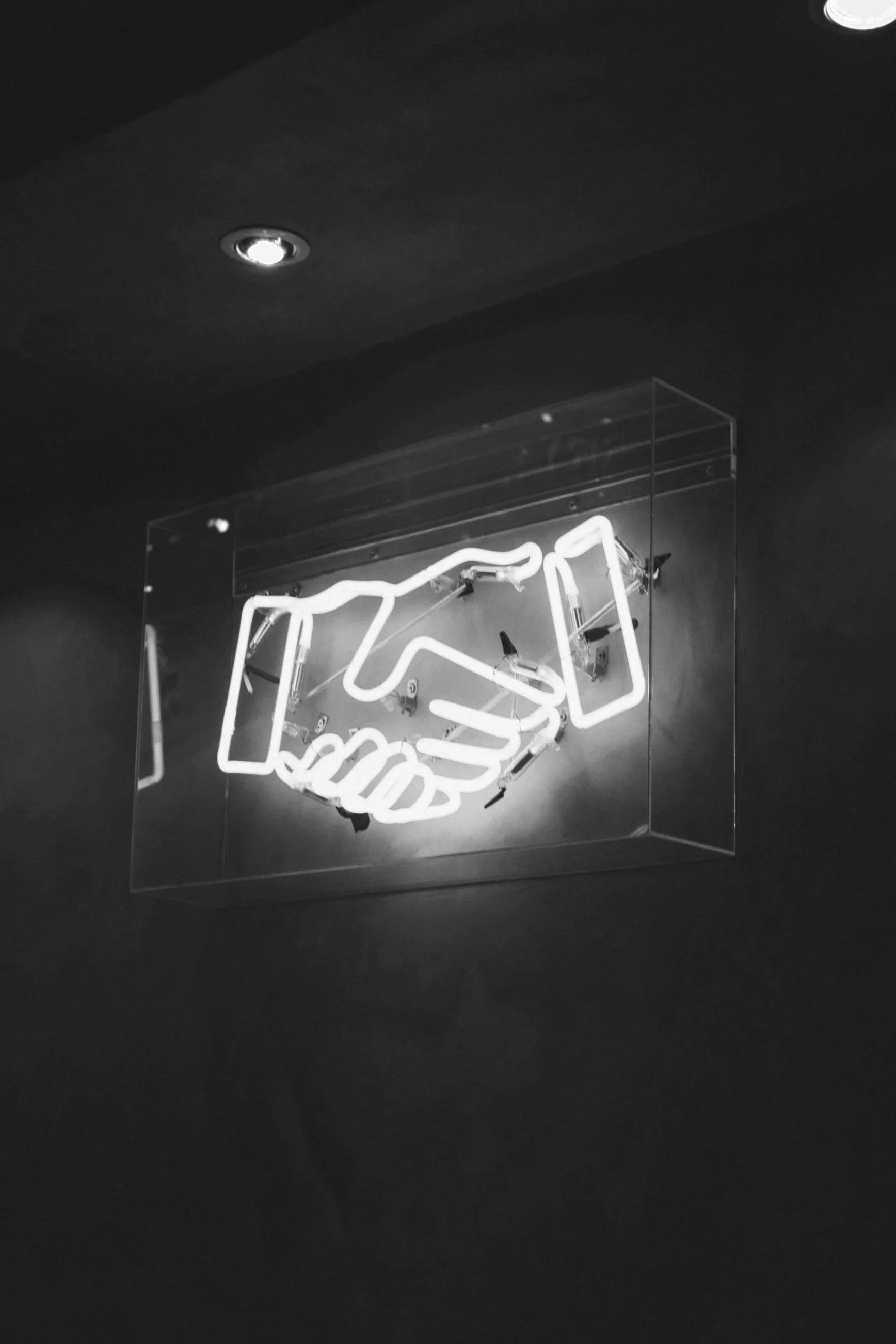 Neon sign of a handshake mounted on a dark wall.