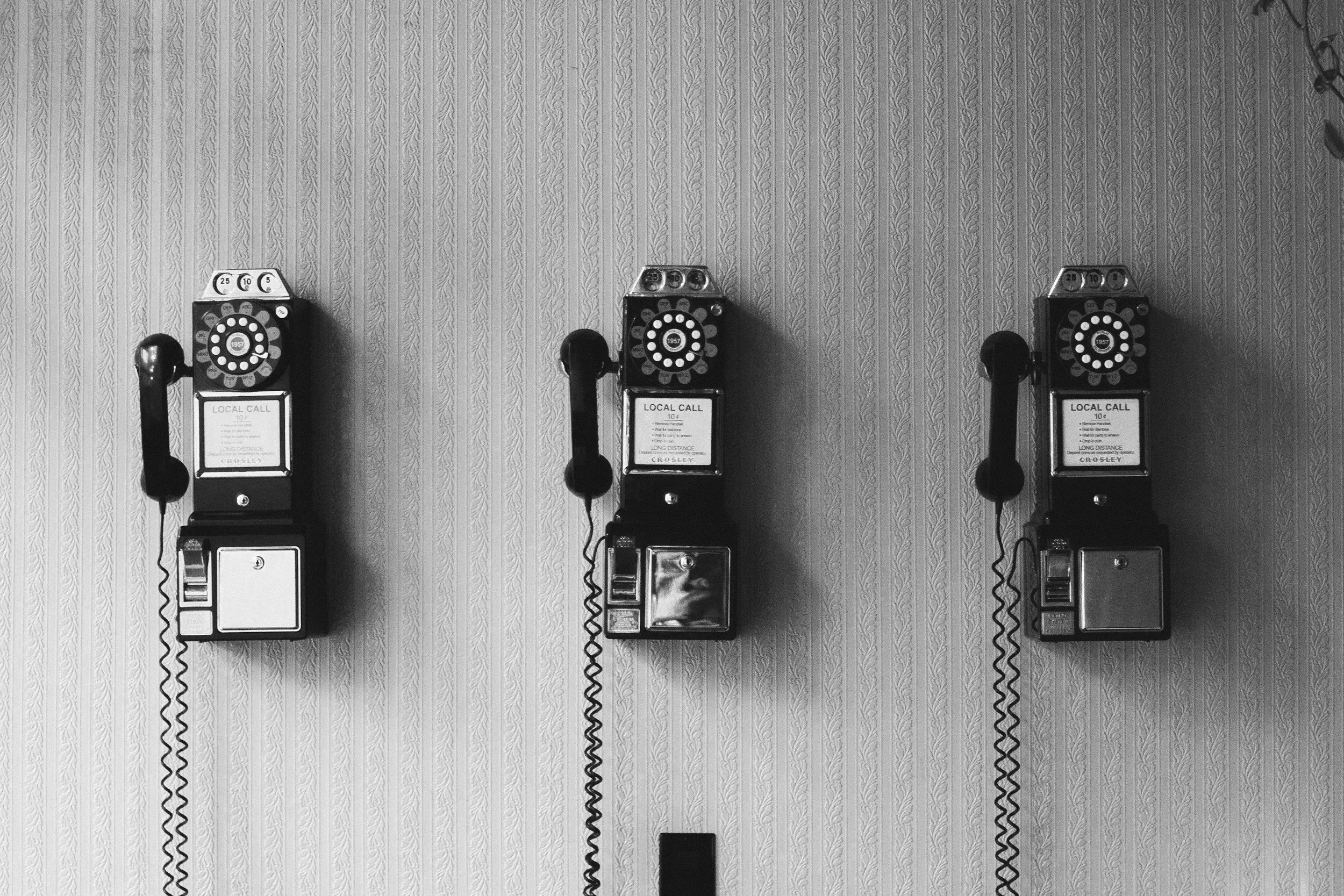 Three vintage payphone phones mounted on a patterned wall.