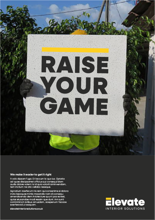 Person holding a sign that says 'RAISE YOUR GAME' in front of foliage and a building.