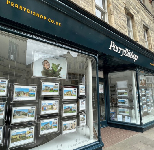Front of Perry Bishop real estate office with display windows showcasing property listings on the street.