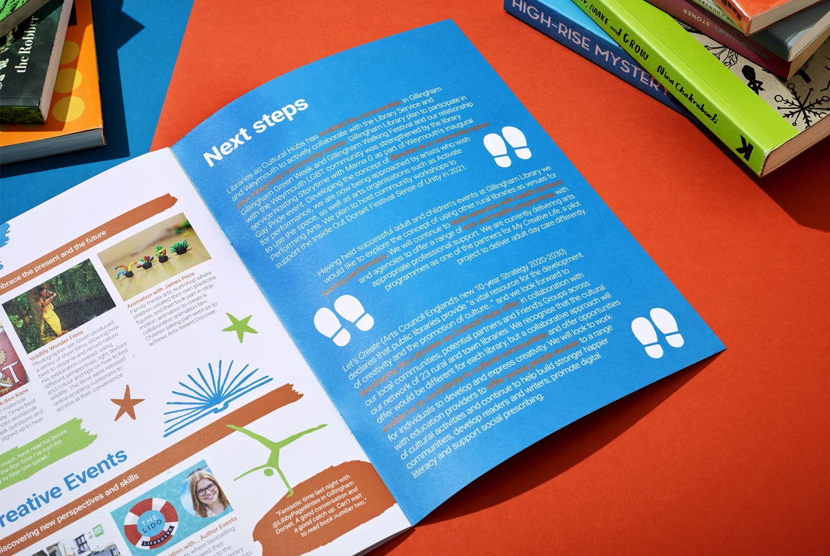 An open booklet on a orange surface with colorful illustrations and text. The right page has a section titled 'Next steps' with text about local cultural and community programs. The left page displays images related to creative events, with colorful star and tree illustrations underneath.