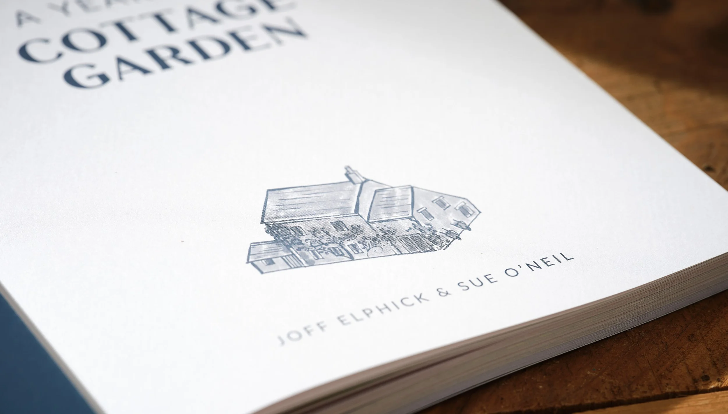 Close-up of a book titled 'A Cottage Garden' with a line drawing of a house on the cover. The authors' names, Joff Elphick and Sue O'Neill, are at the bottom.