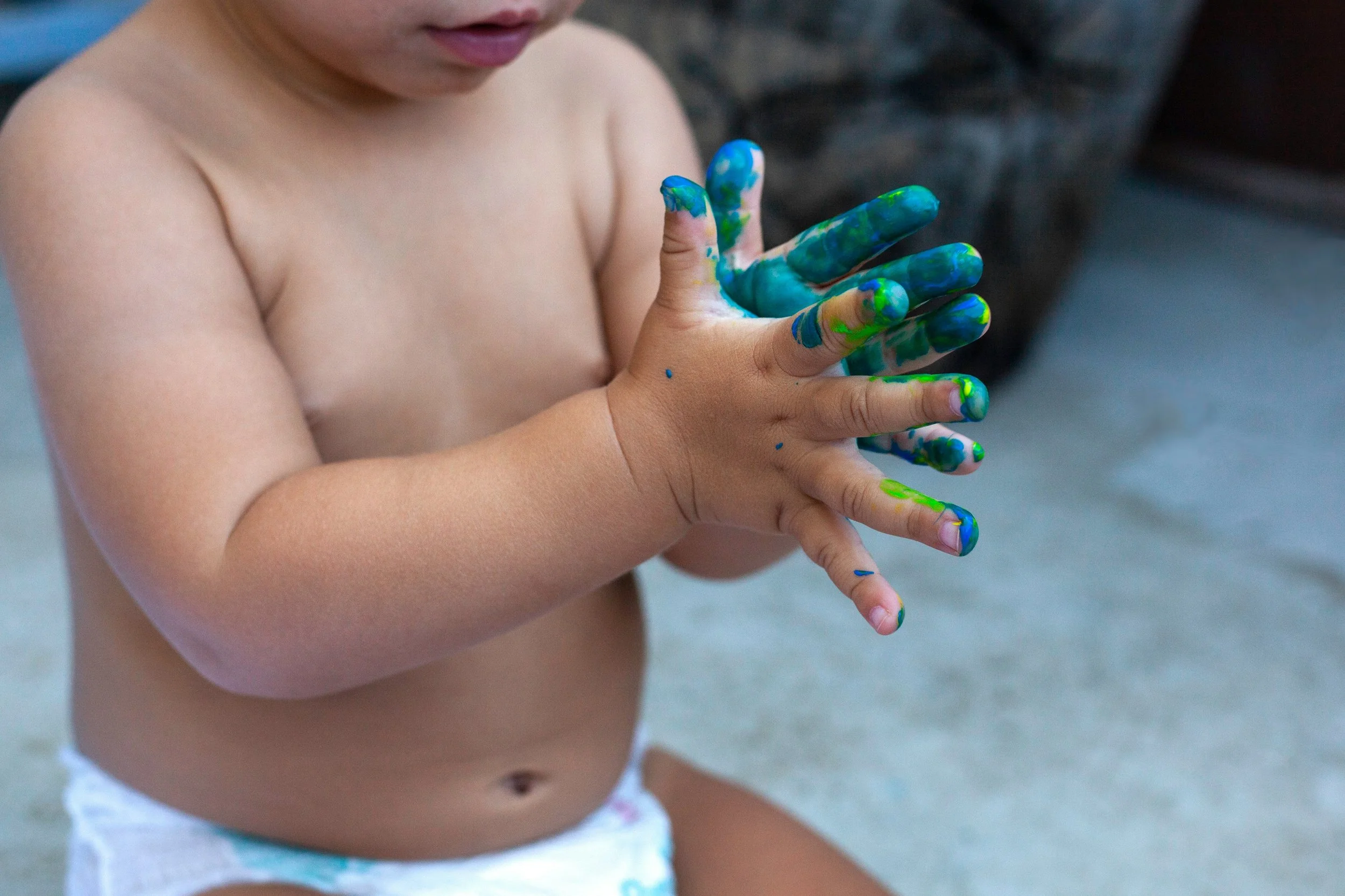 A young child with painted hands demonstrating finger painting, with paint on their fingers and hands.