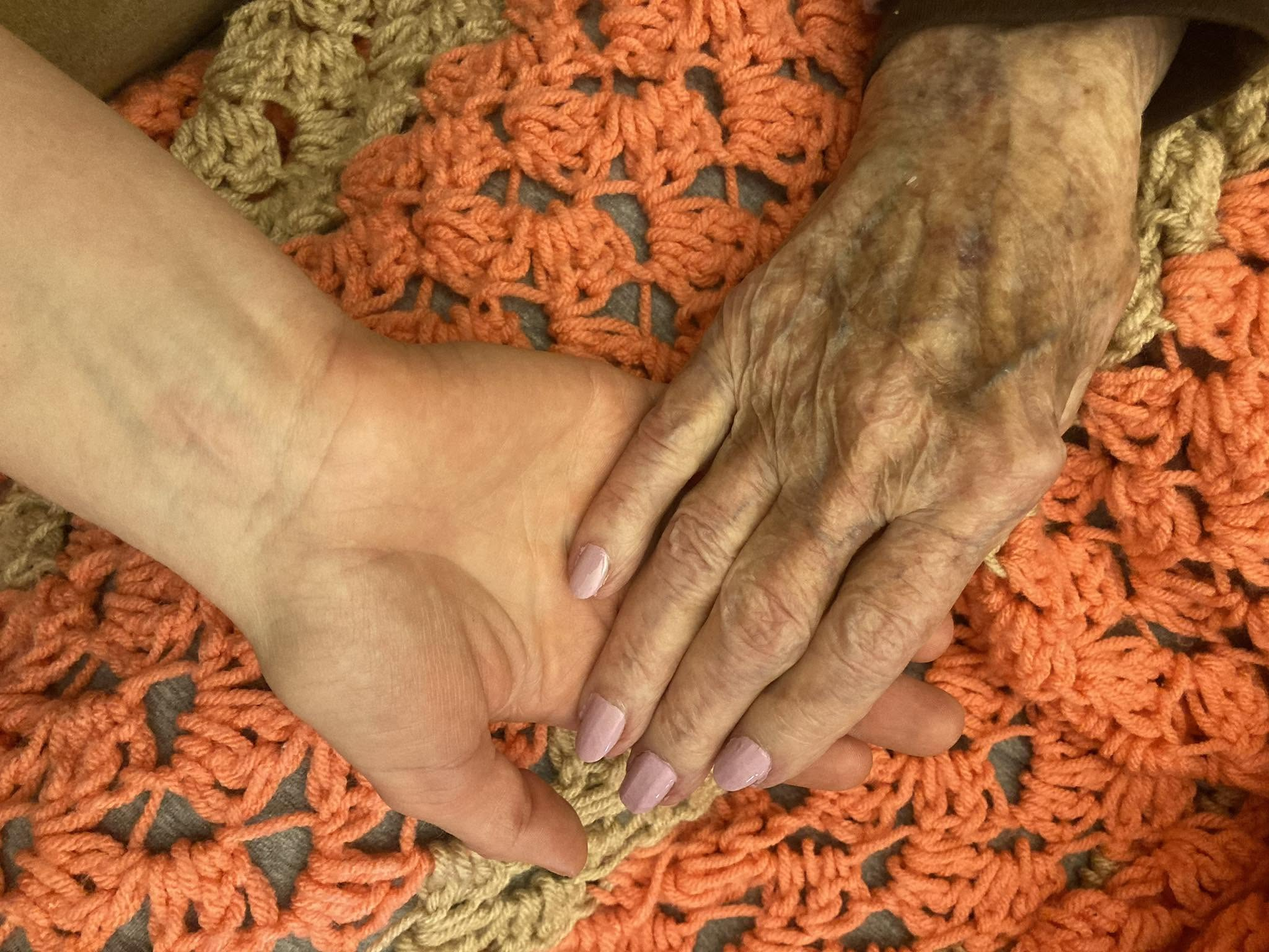 Clarice’s hand resting in a younger hand over a crocheted blanket