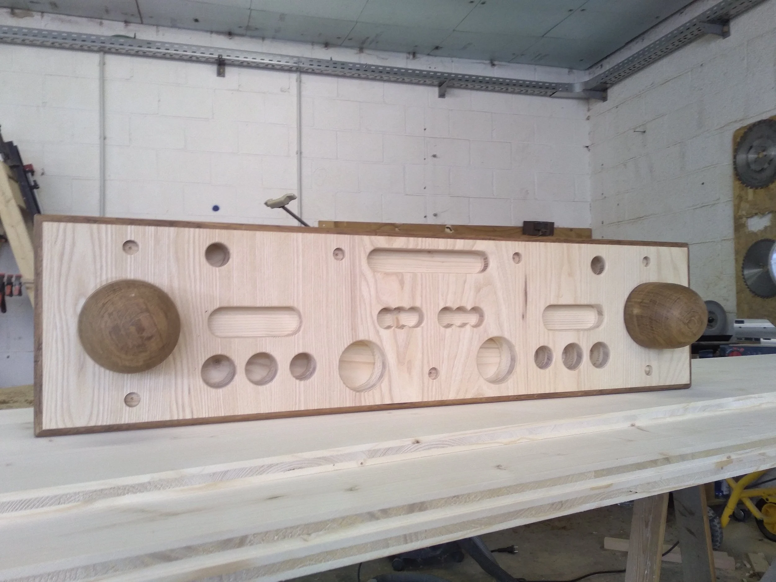 Terrasse en bois avec un mobilier de table et chaises en plastique noir, une grande plante en pot, une maison en briques, et un jardin vert avec des arbres et une balançoire.