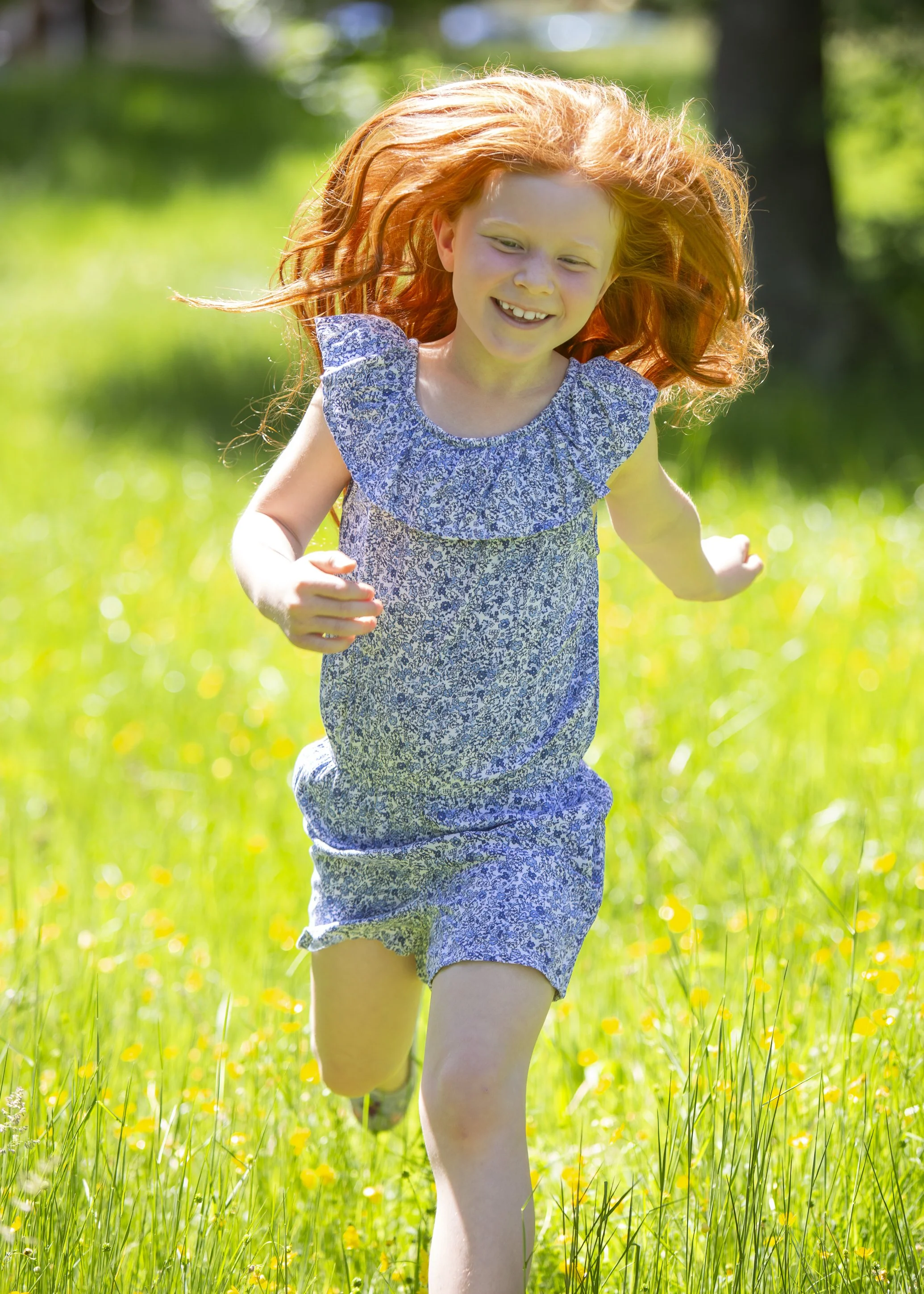 A young girl with red hair running through a grassy field on a sunny day.