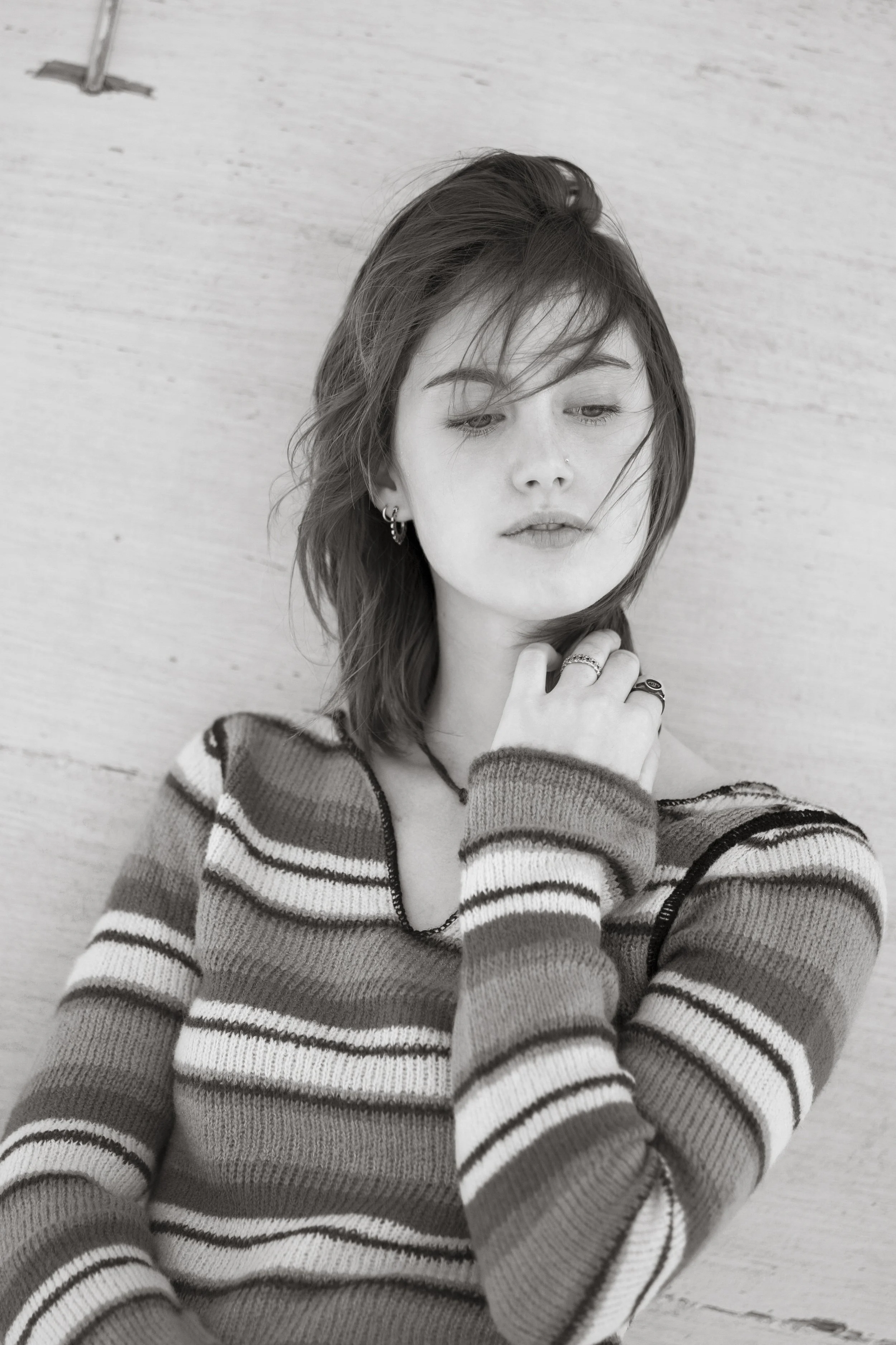 A young woman with short hair and earrings, dressed in a striped sweater, looking down thoughtfully while lying on a wooden floor.