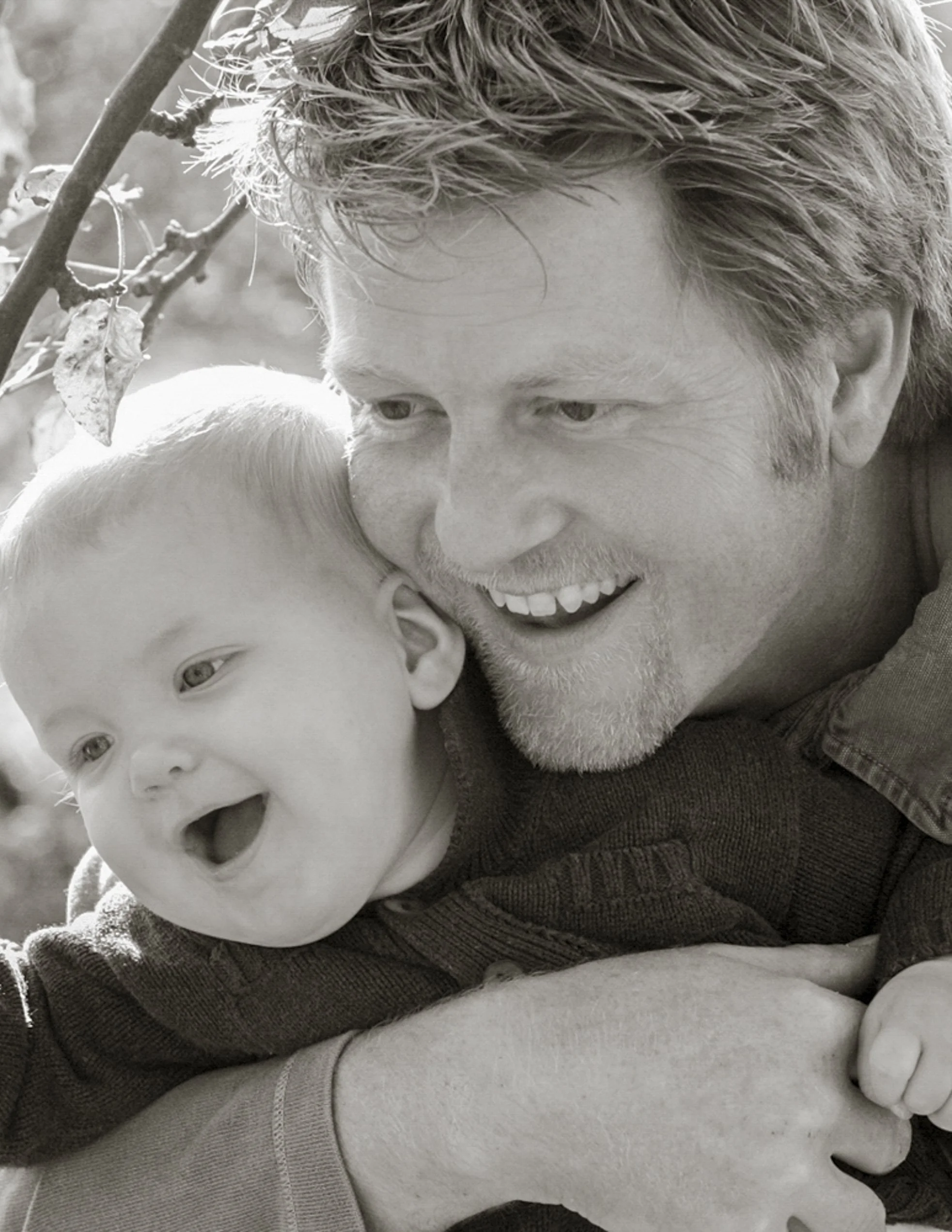 A man and a young child are close together, smiling and enjoying each other's company outdoors.