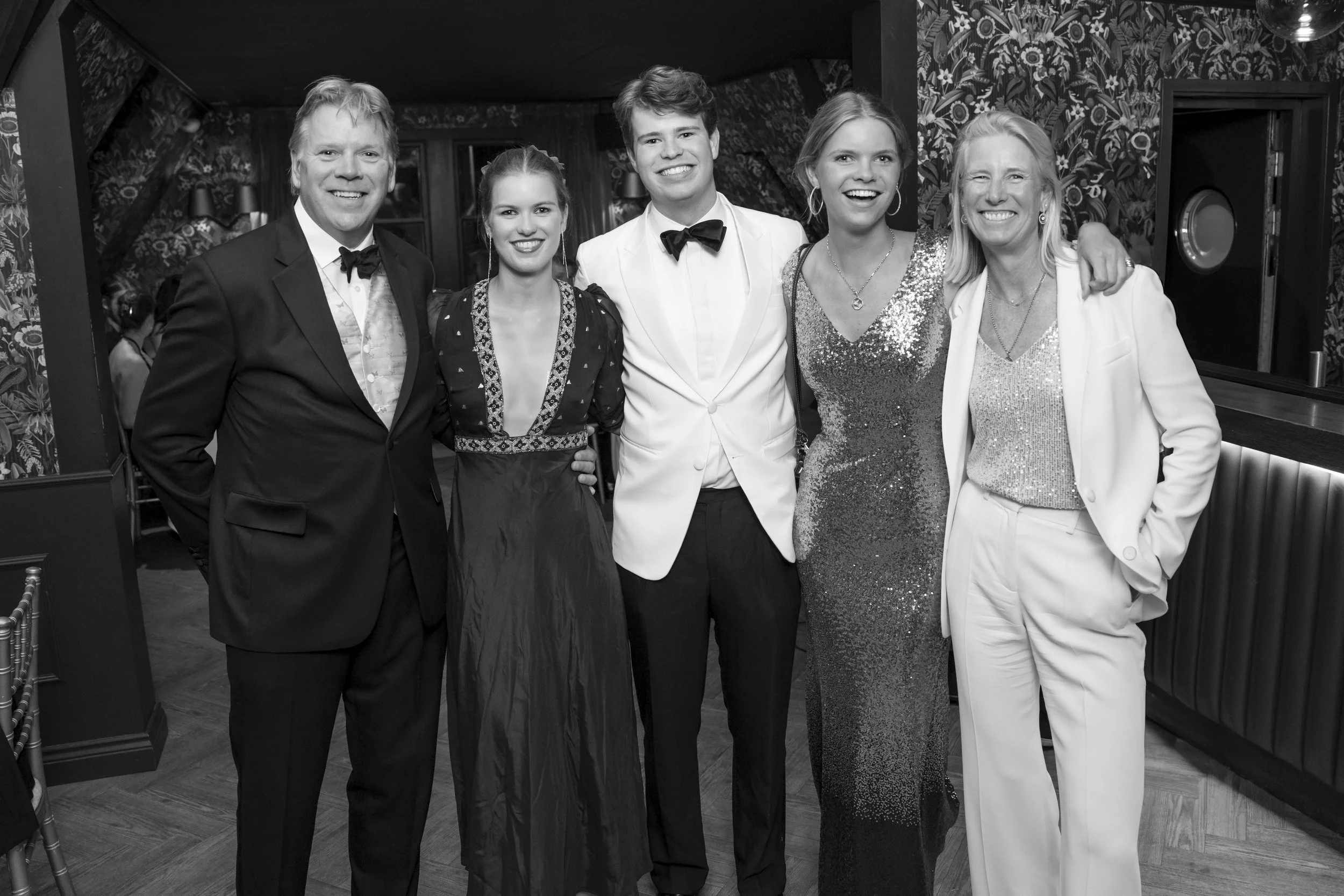 Group of six people in formal evening attire posing together at an event.