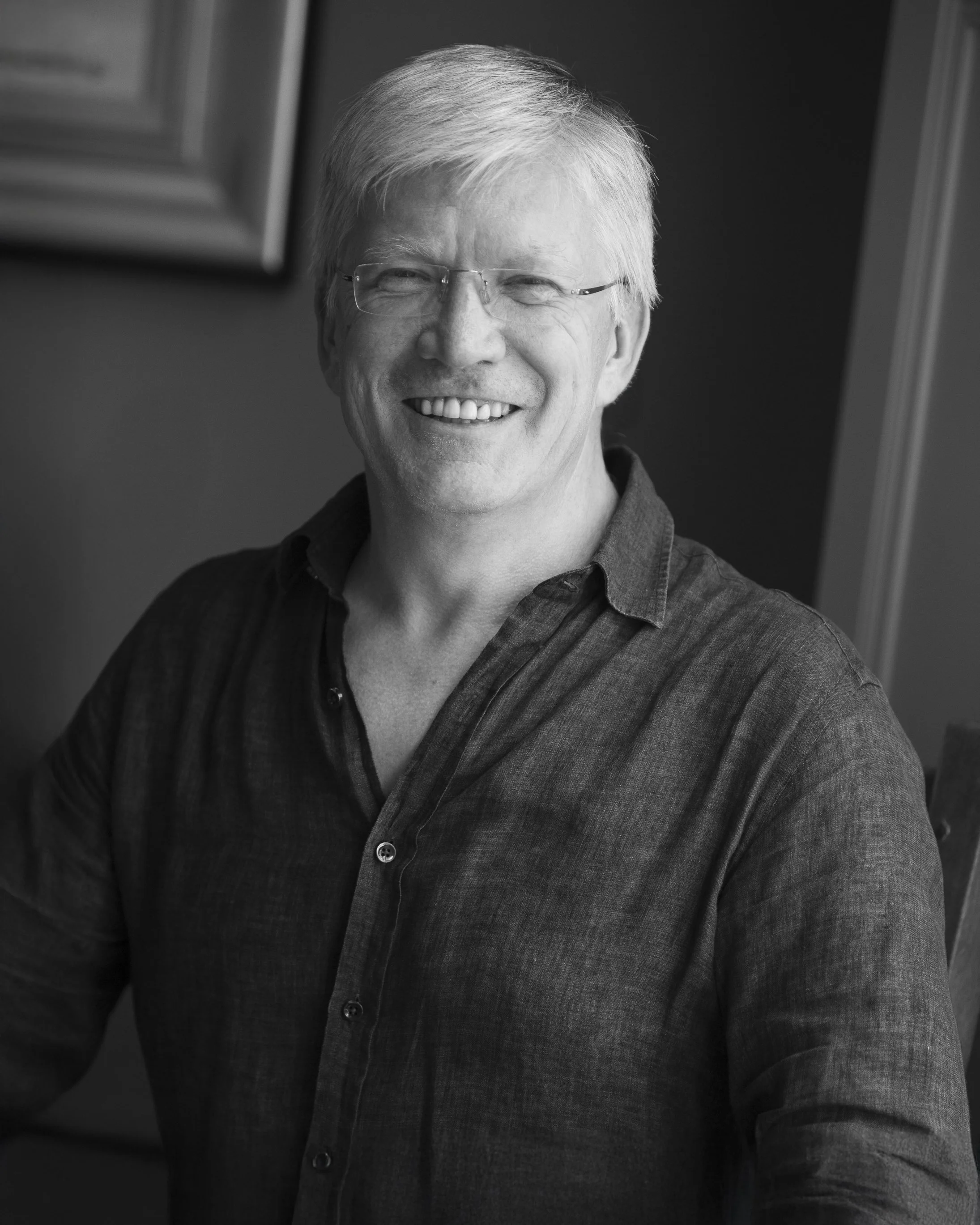 A smiling middle-aged man with light hair and glasses, wearing a casual button-up shirt, in a black and white portrait.
