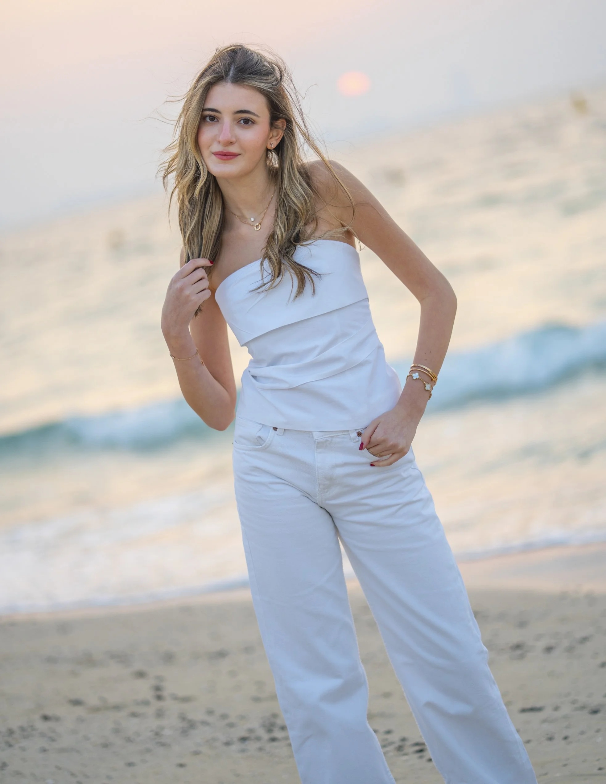 A young woman in white clothing standing on a beach at sunset