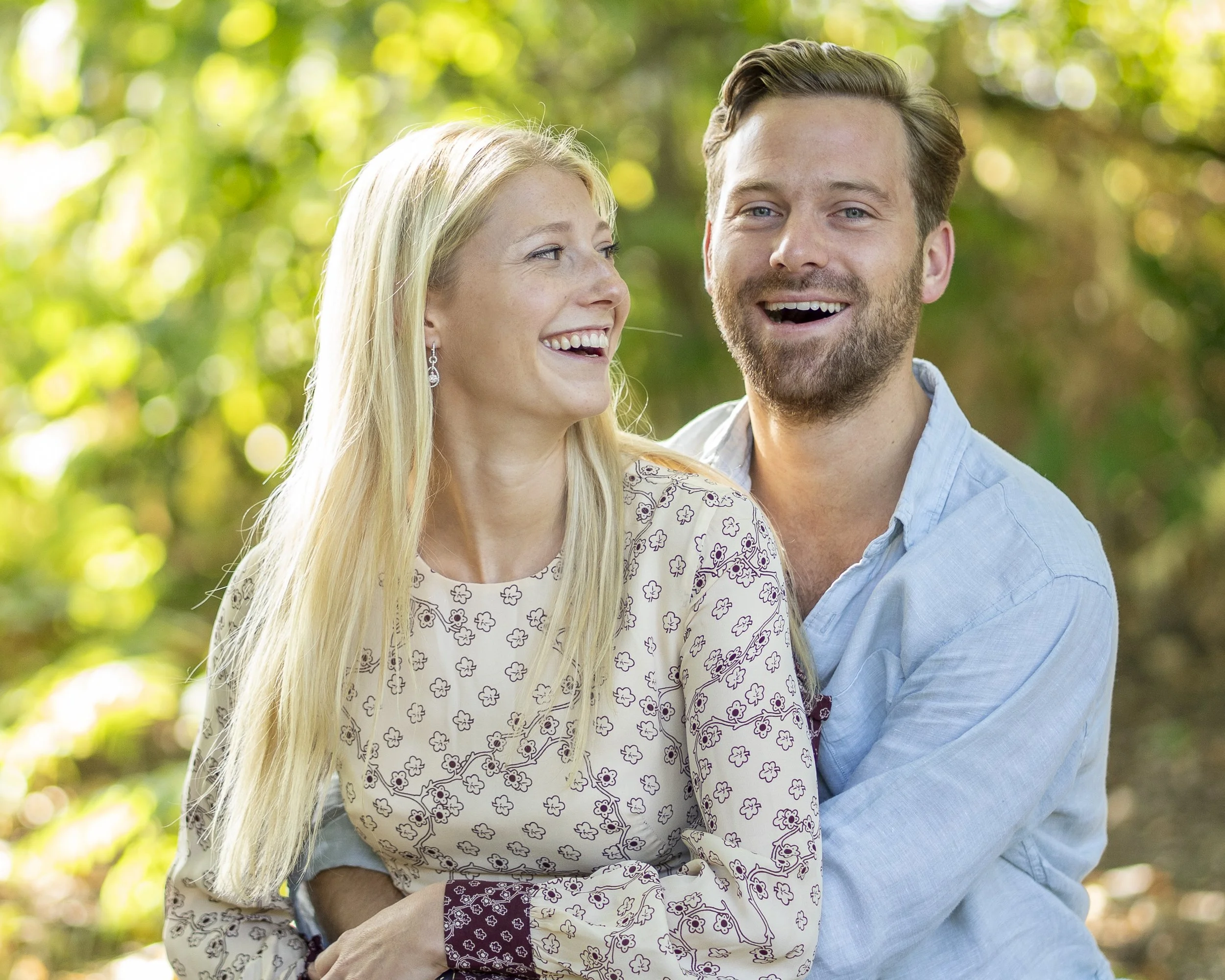 A couple laughing and enjoying each other's company outdoors in a sunny, green park.