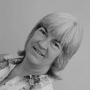 Black and white photo of a smiling woman with short, layered hair, wearing a patterned top.