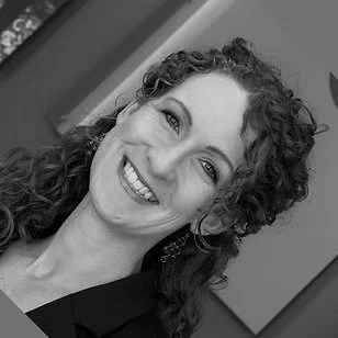 Close-up black and white photo of a woman with curly hair smiling.