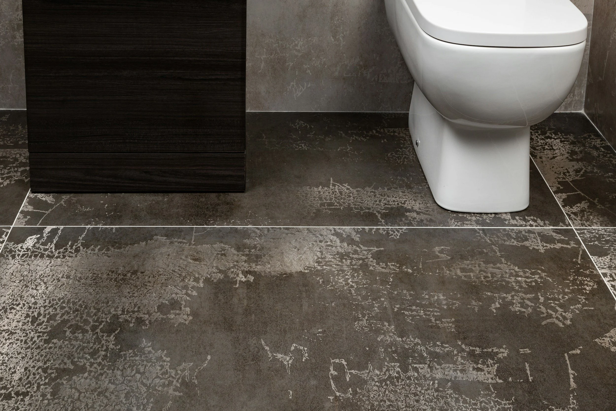 Bodenfliesen in dunkler, strukturierten Optik, Badezimmer mit weißem WC und dunklem Holzmöbel
