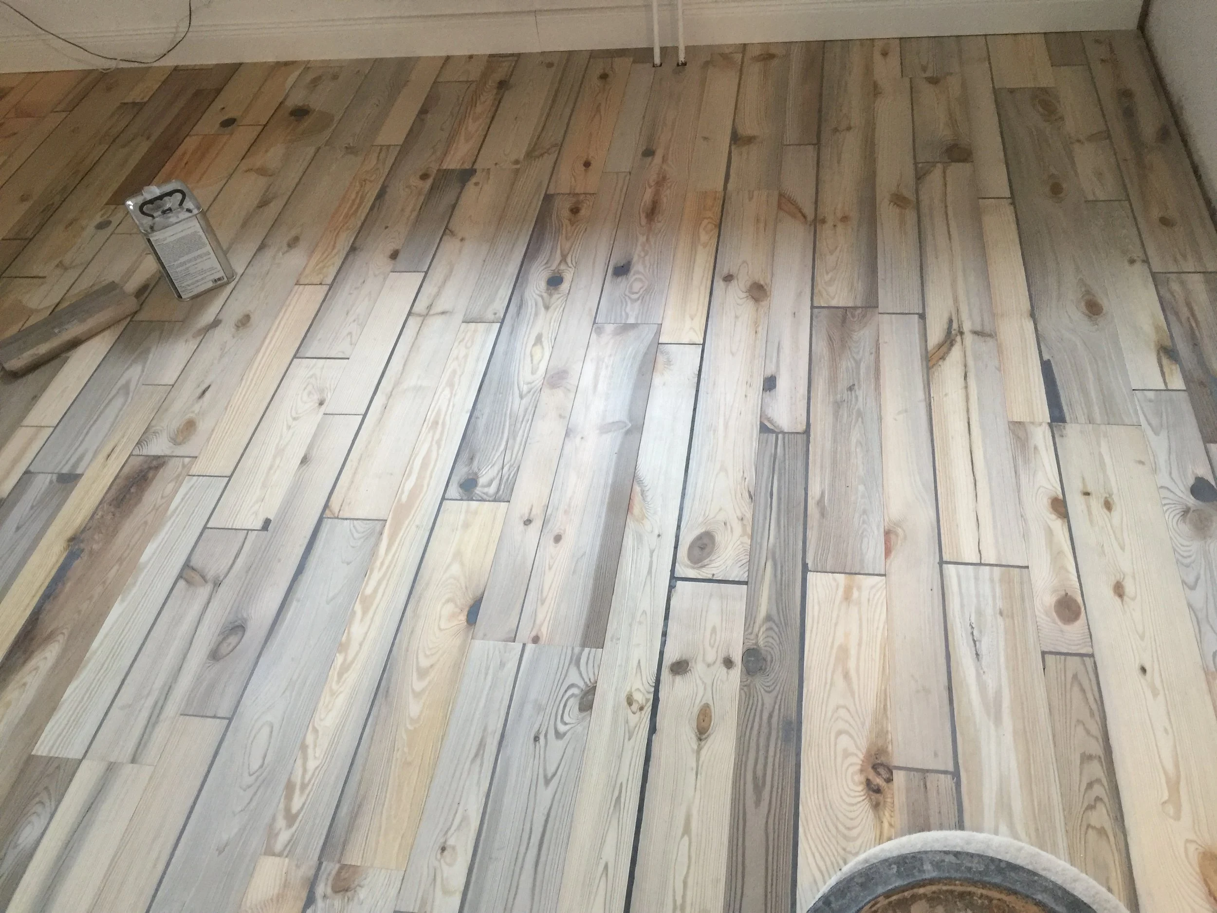 Holzboden, der gerade verlegt wird, mit Werkzeug und Klebeband auf dem Boden.