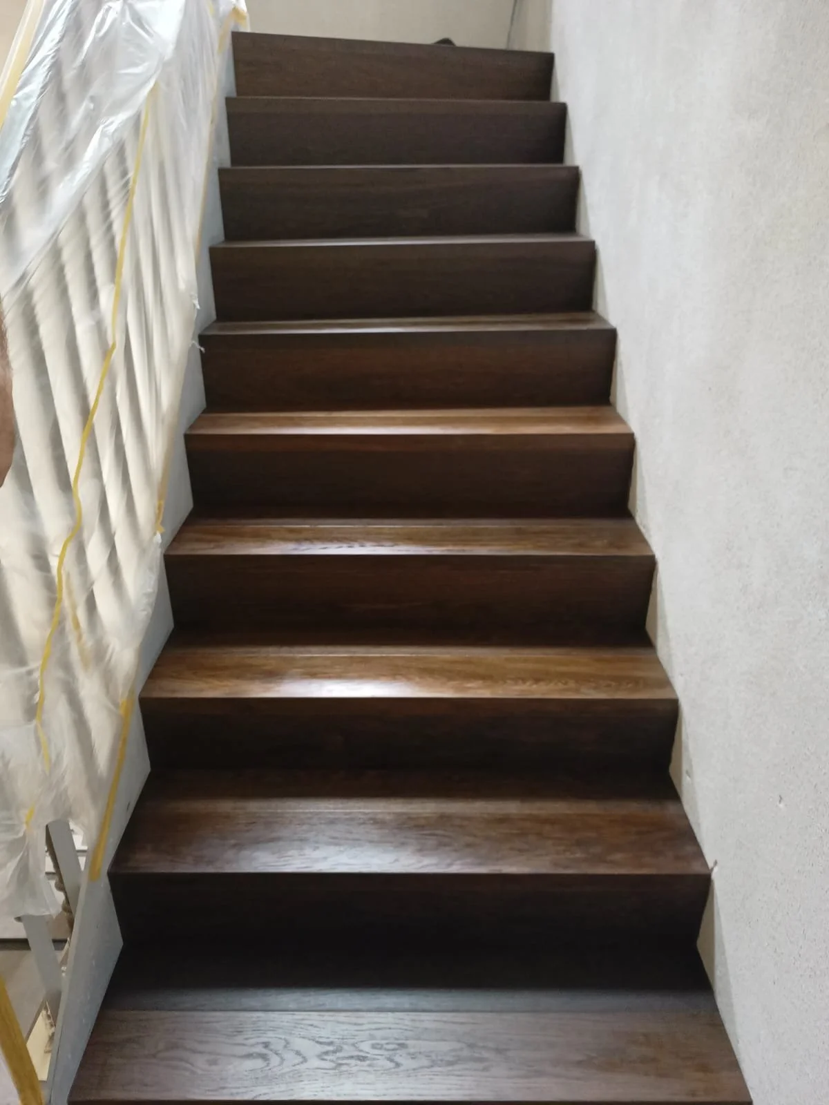 Holztreppe im Innenbereich mit weißen Wänden, Schutzfolie an der Seite.