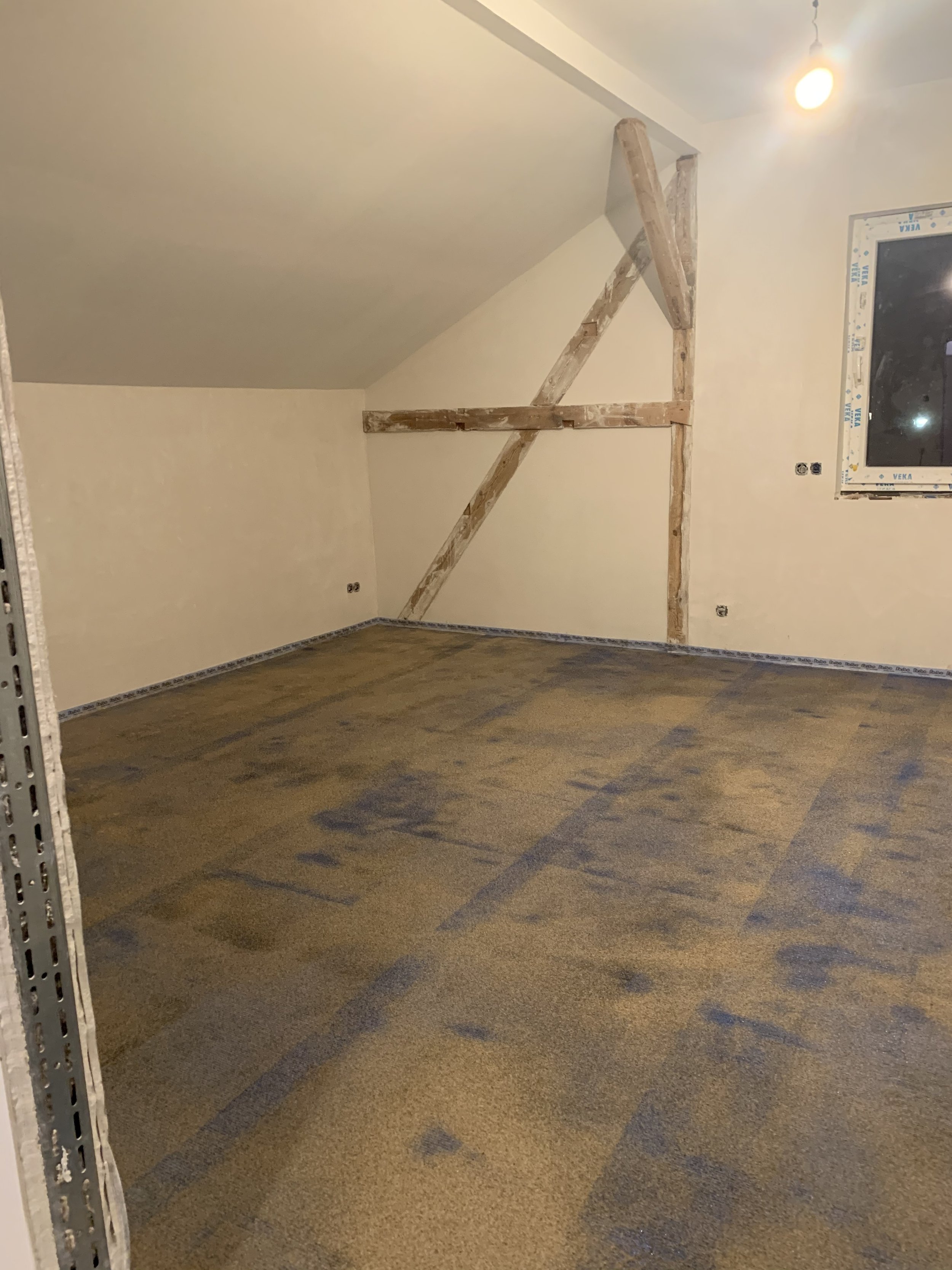 Unfertig renoviertes Zimmer mit Dachschräge, Holzstützstreben und einem Fenster