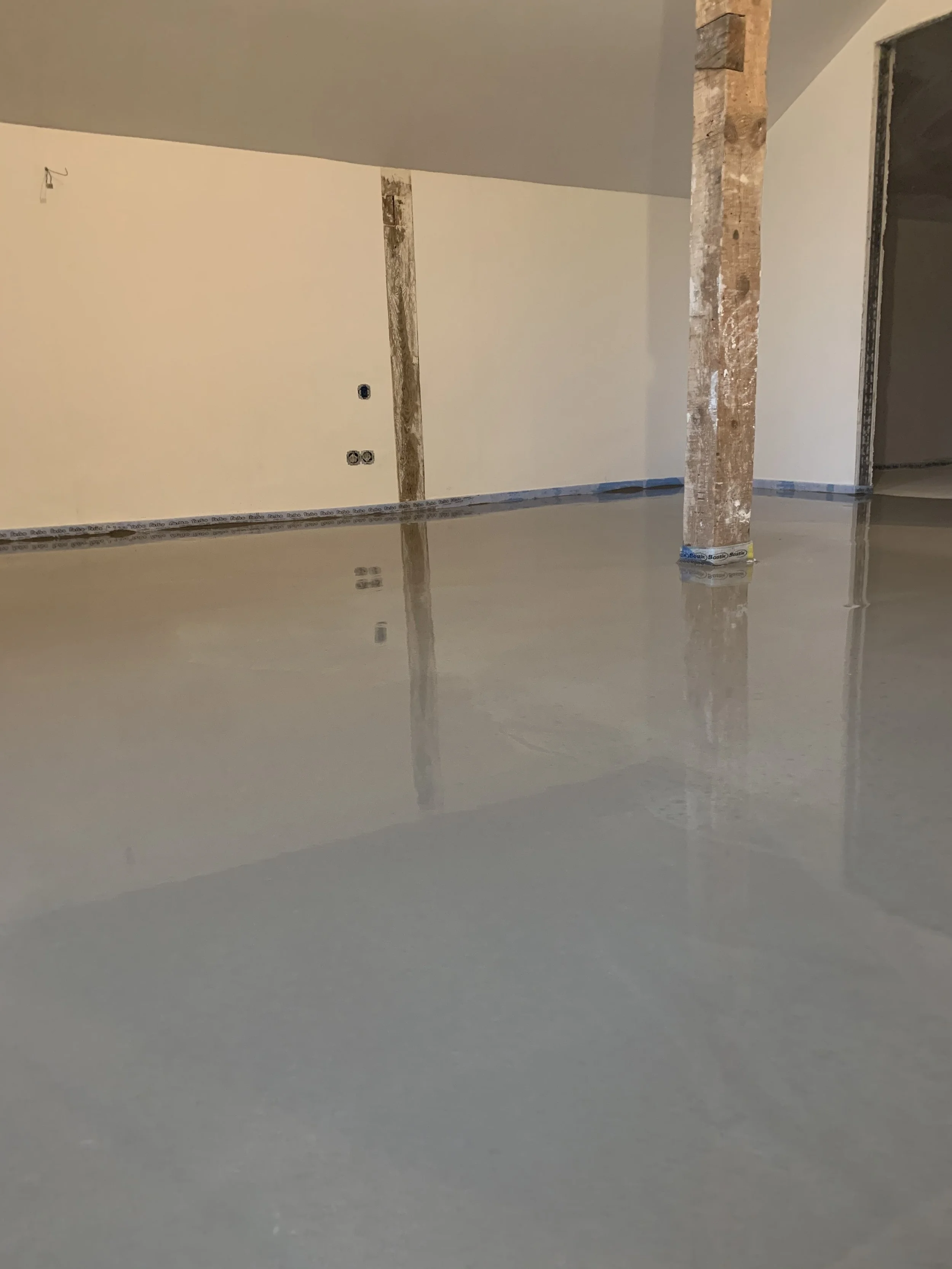 Ein noch im Bau befindliches Zimmer mit einer frisch gegossenen, glänzenden Betondecke, Baugerüste und offene Wände.