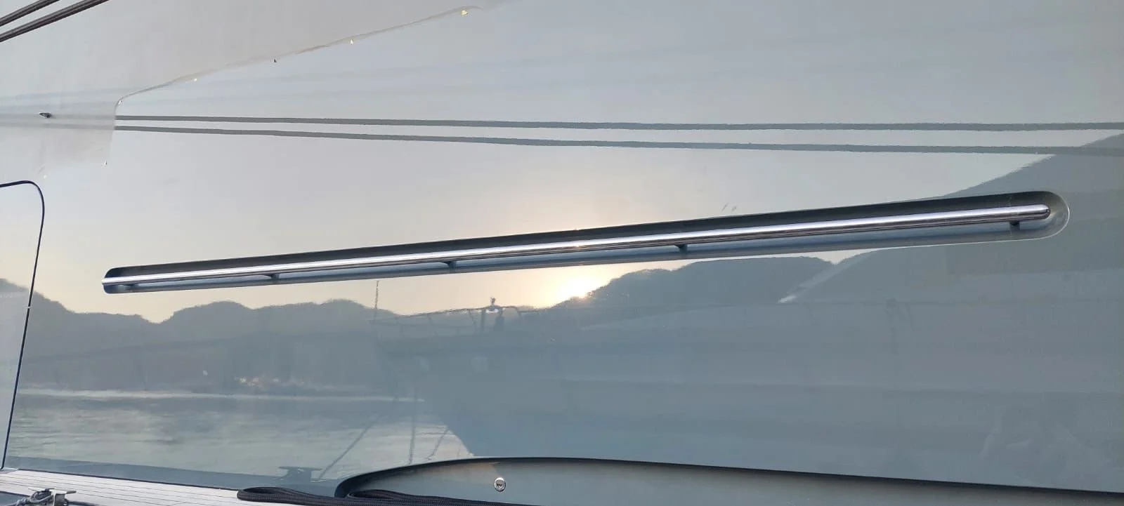 Close-up of a boat's exterior with a chrome rail and reflection of hills and sky.
