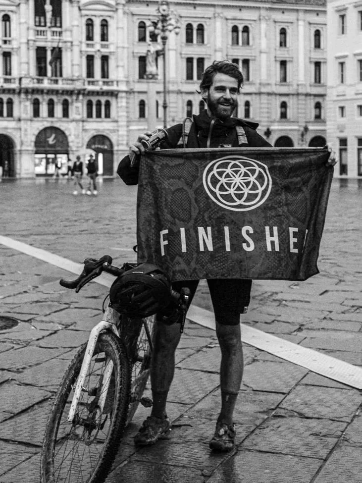 Cyclist holding a bike and finisher flag after an endurance event – symbolizing the connection between bike fitting and performance at Timo Bikefit Munich.