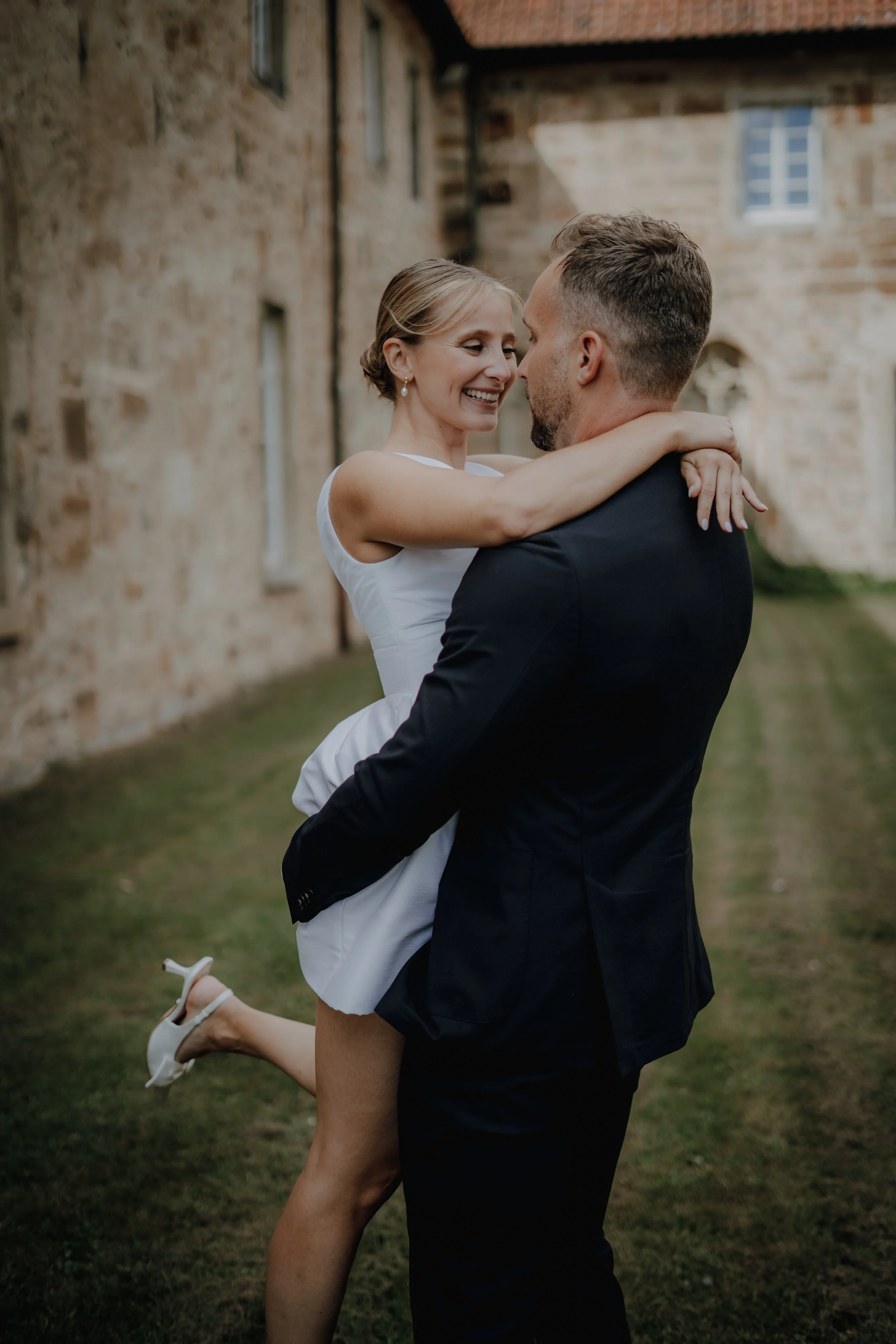 Ein glückliches Paar bei einer Hochzeit, das sich umarmt und lächelt, vor einem alten Steingebäude.
